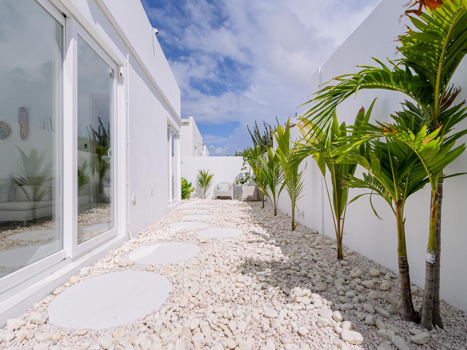 Pathway on the side of the home with round pavers to lead the way through the white caribbean beach pebble stone layout - Palm trees and tropical plants enhance the vacation feel