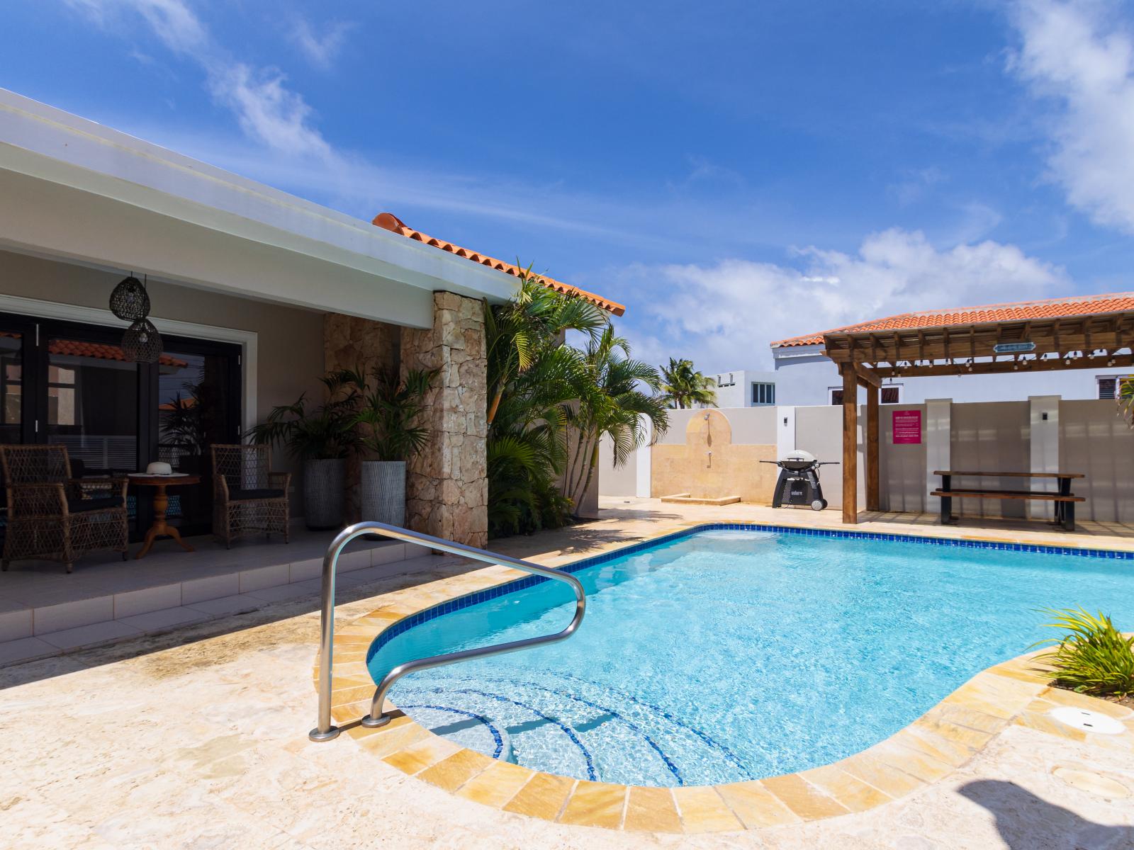 Captivating Pool Area of the Apartment in Noord Aruba - A spot for friends and family to gather and socialize - Palm trees and tropical plants enhance the vacation feel - Pool Area with shaded outdoor seating option
