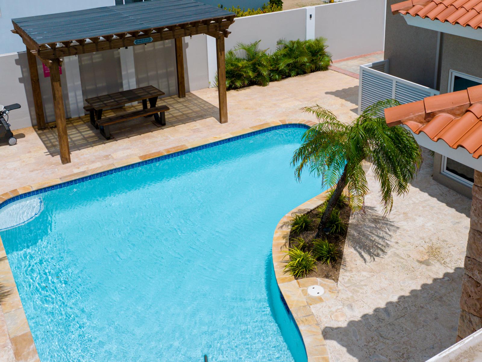 Captivating Pool Area of the Apartment in Noord Aruba - A spot for friends and family to gather and socialize - Palm trees and tropical plants enhance the vacation feel - The spacious backyard provides ample room for relaxation