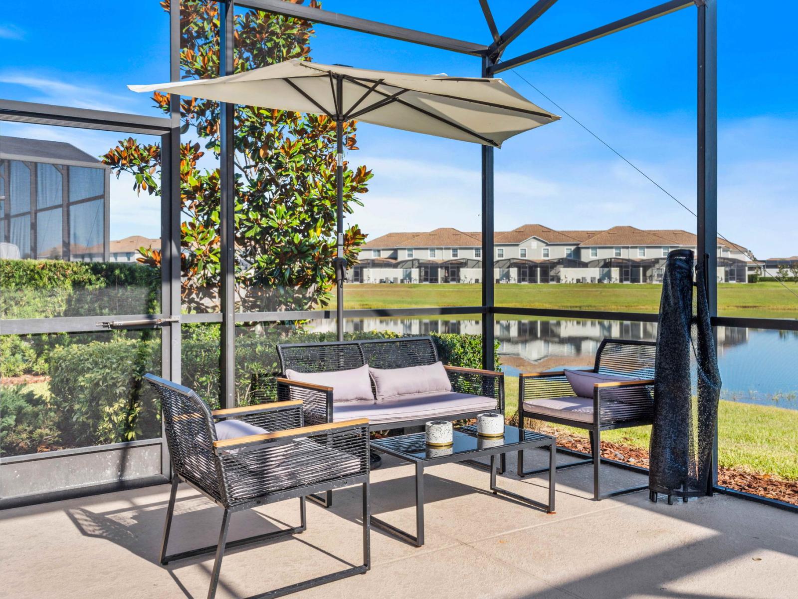 Outdoor seating area by the pool with lake views of the home in Kissimmee Florida - Featuring a shaded umbrella - Savoring a morning coffee or soaking up the afternoon sun - This inviting space provides the perfect setting to relax and unwind