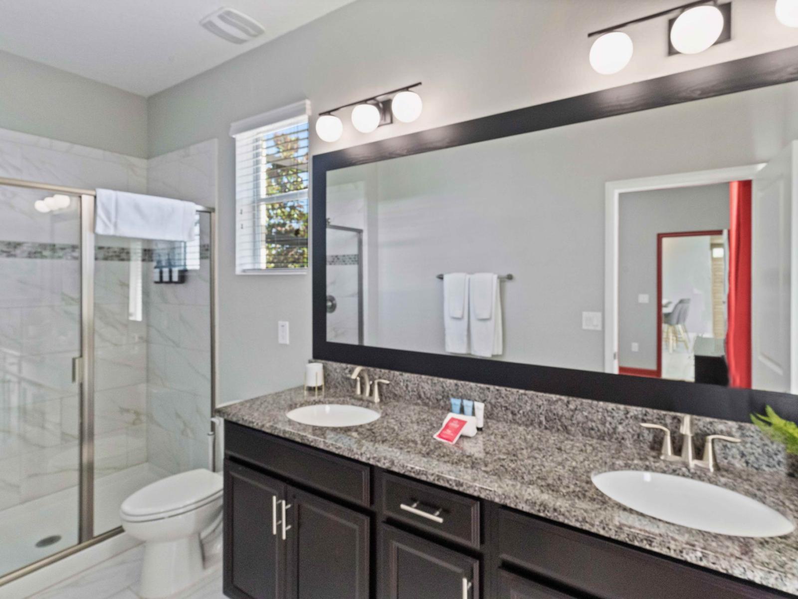 Polished bathroom of the home in Kissimmee Florida - Elegant bathroom with luxurious fixtures and finishes - Chic dual vanity with large mirror and upscale lighting - Spacious glass-enclosed walk-in shower area