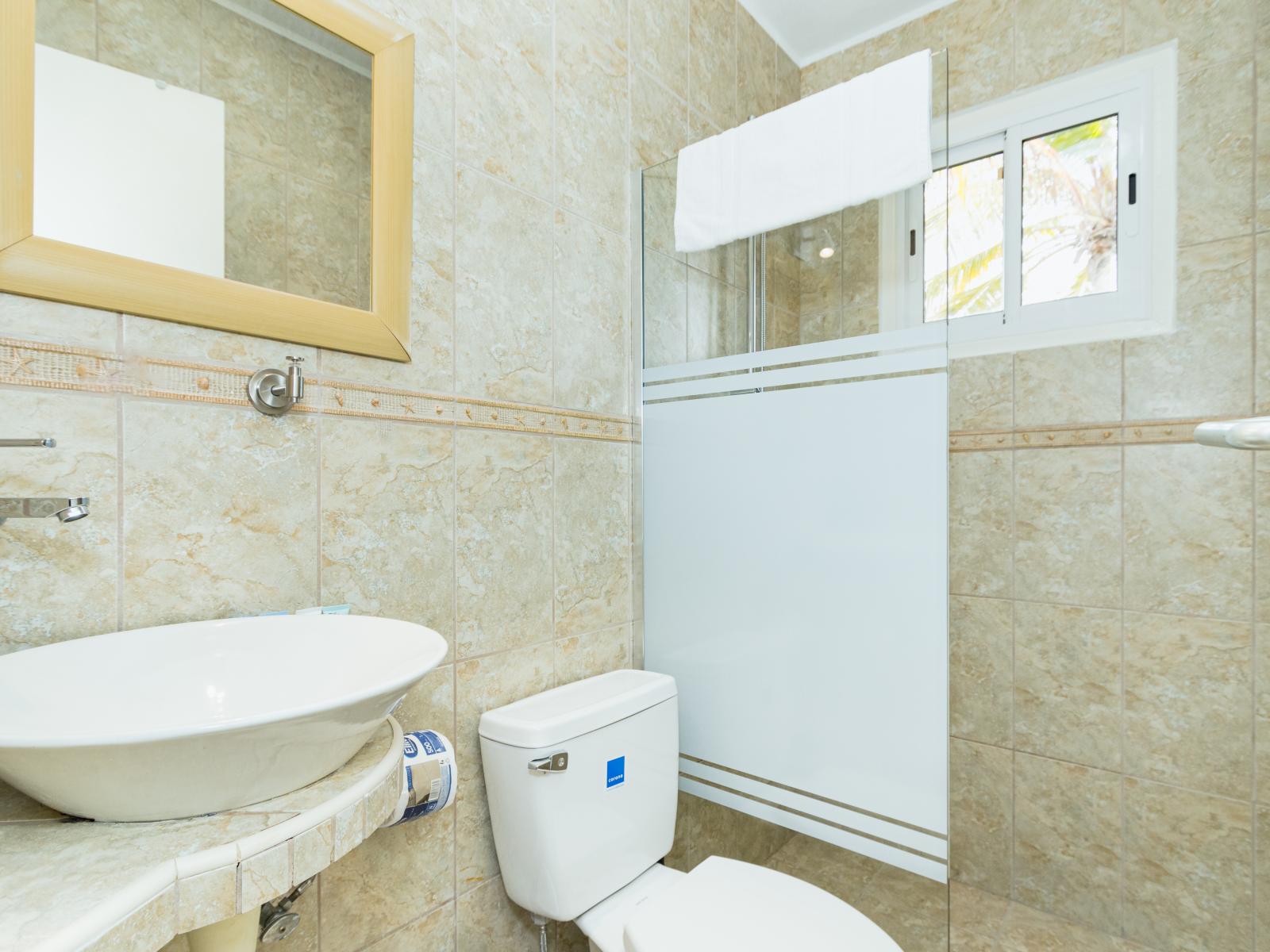 Classical Bathroom of the villa in Noord, Aruba - Neat and clean toilet seat - Availability of all bathroom amenities - Beautiful vanity with large size wall mirror  - Elegant lighting - Stunning separate glass partitioned shower area