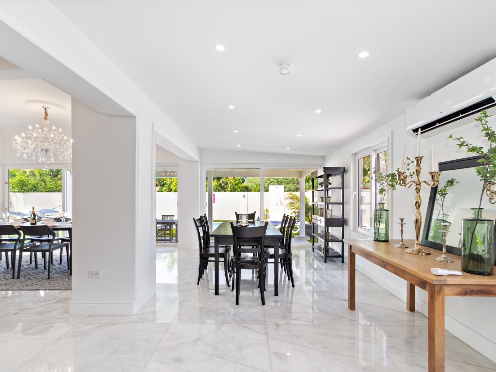 Amidst the dining area's decor with green plants, there's a seamlessly integrated air conditioning unit, providing a comfortable atmosphere. Moreover, the sliding door offers a view of the backyard pool, enhancing the overall charm of the space.