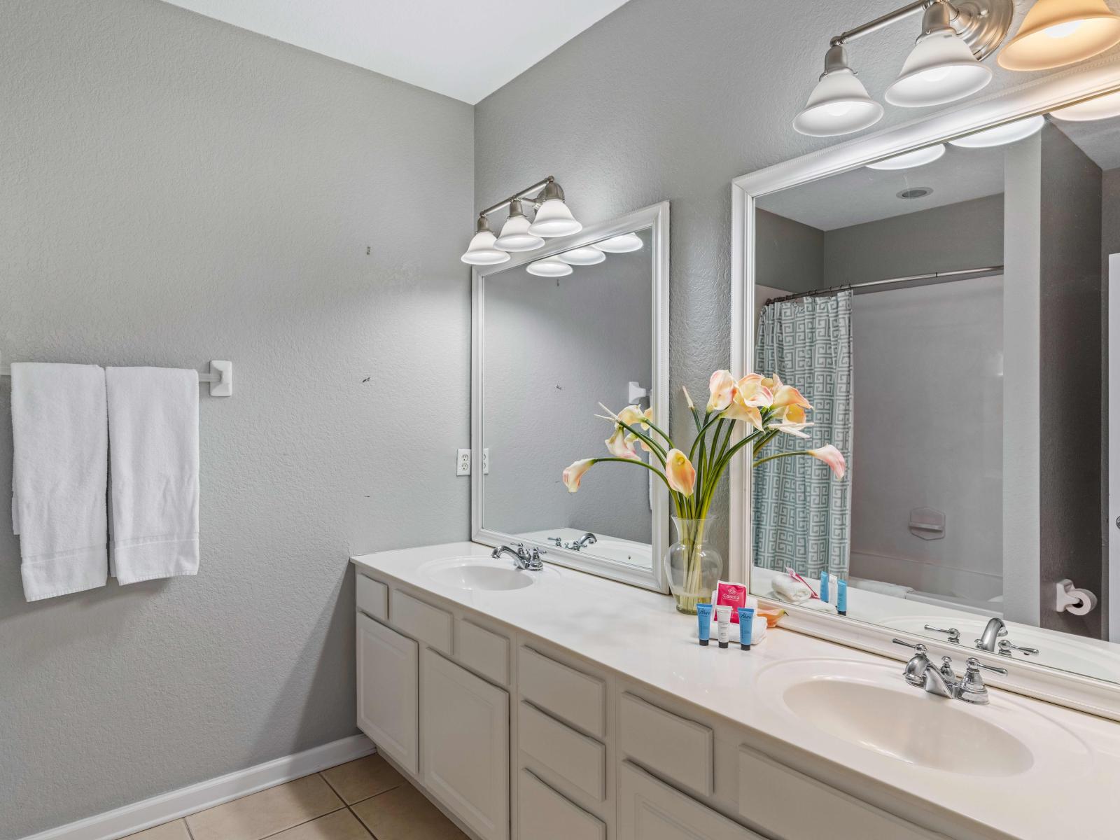 En-suite bathroom of the townhouse in Orlando - Featuring a  double sink vanity with twin big size wall mirrors and lamps for elegant lighting - Freshen up yourself in the well designed bathtub/shower combination - Availability of all amenities