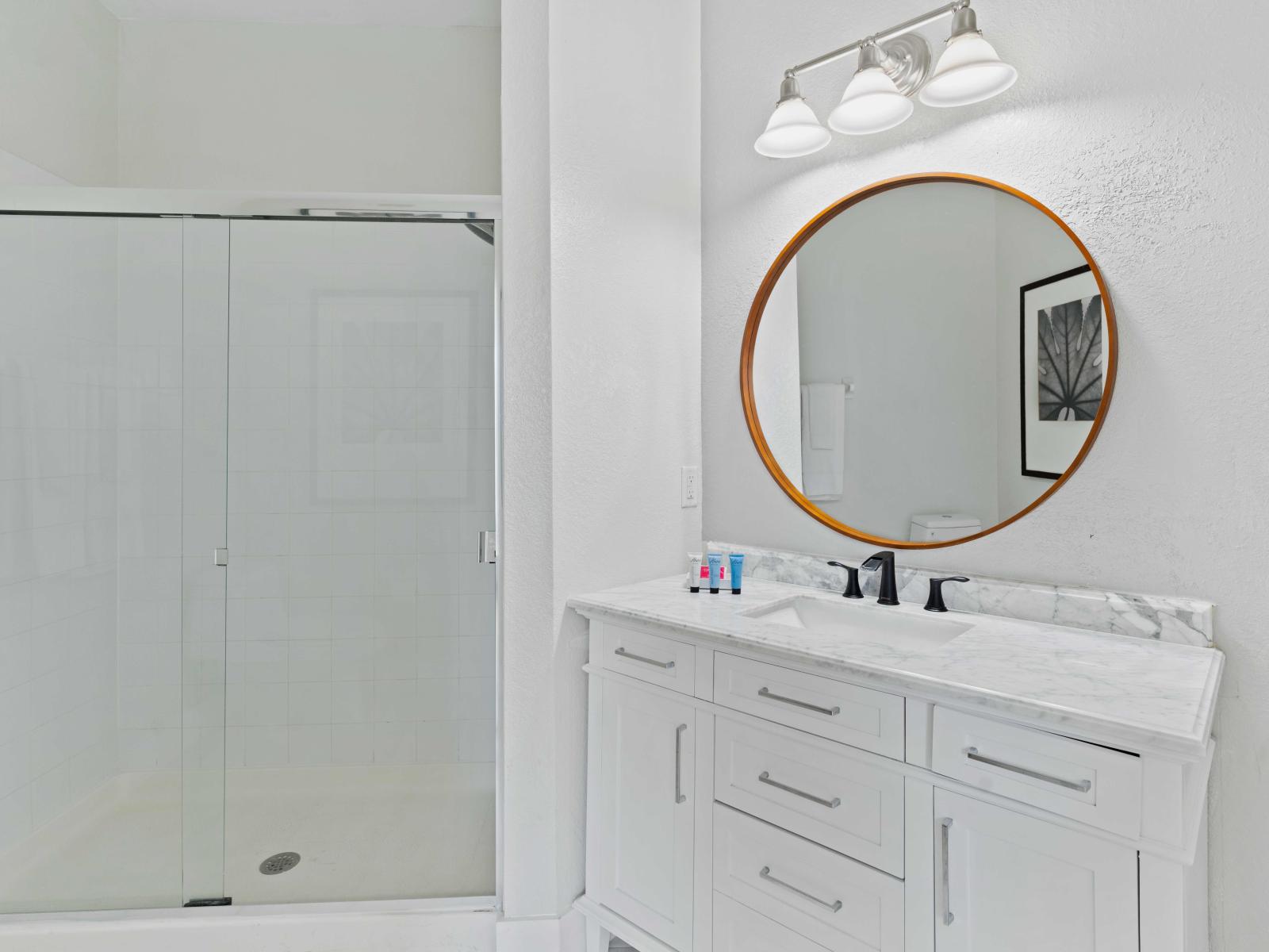 Experience modern elegance in our en-suite bathroom, featuring a sleek walk-in shower and a stylish round vanity mirror for added sophistication and convenience.