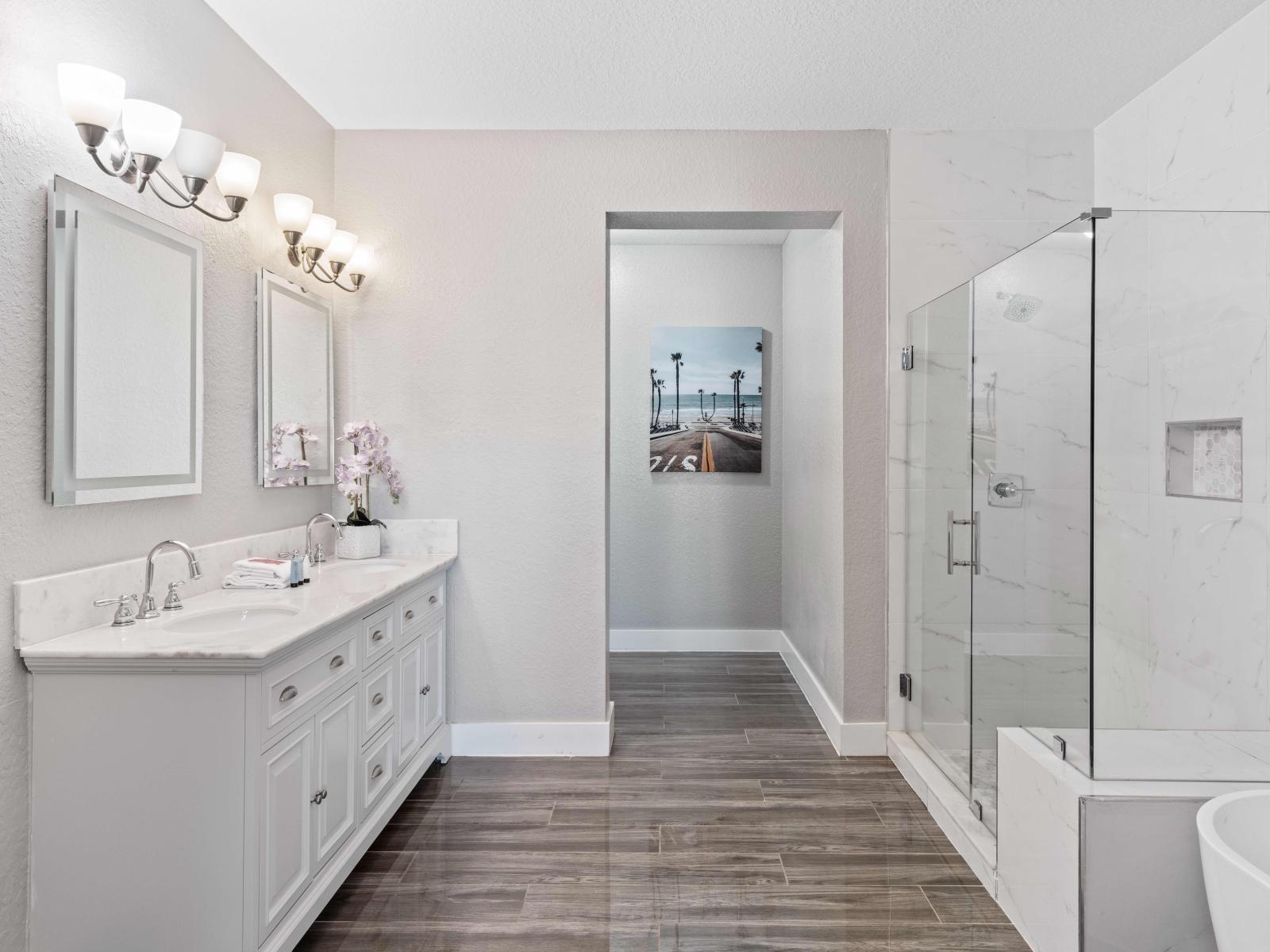 Exclusive bathroom of the condo in Orlando - This area features a sumptuous soaking tub and a spacious walk-in shower - Elegant double sinks vanity with wall mirrors and elegant wall lamps - This opulent space invites you to refresh in style.