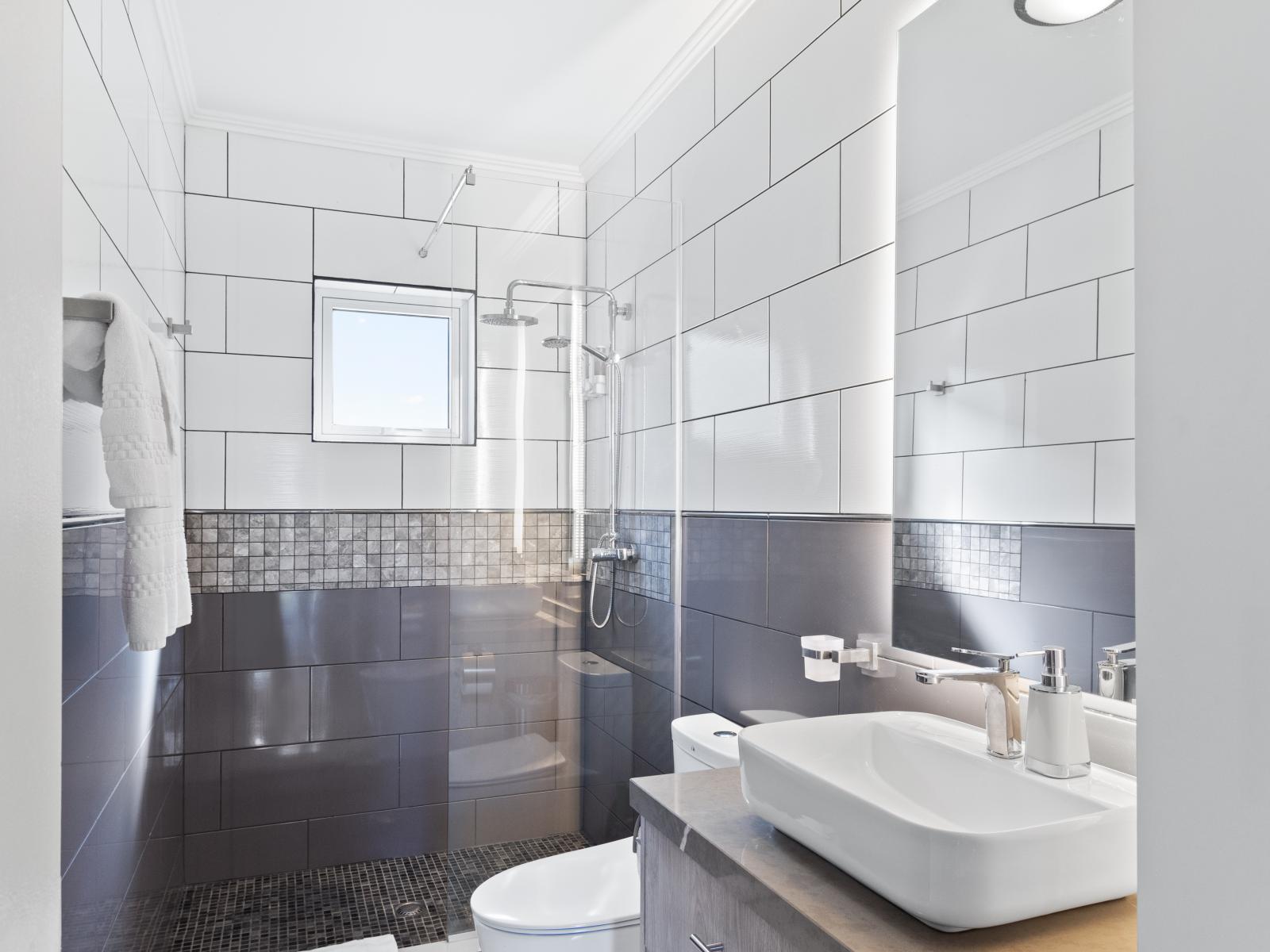 Palatial Bathroom of the Apartment in Noord Aruba - Sophisticated color palette creating a serene ambiance - Ample natural light highlighting the elegant tilework - Seamless design featuring a glass-enclosed shower for a modern touch