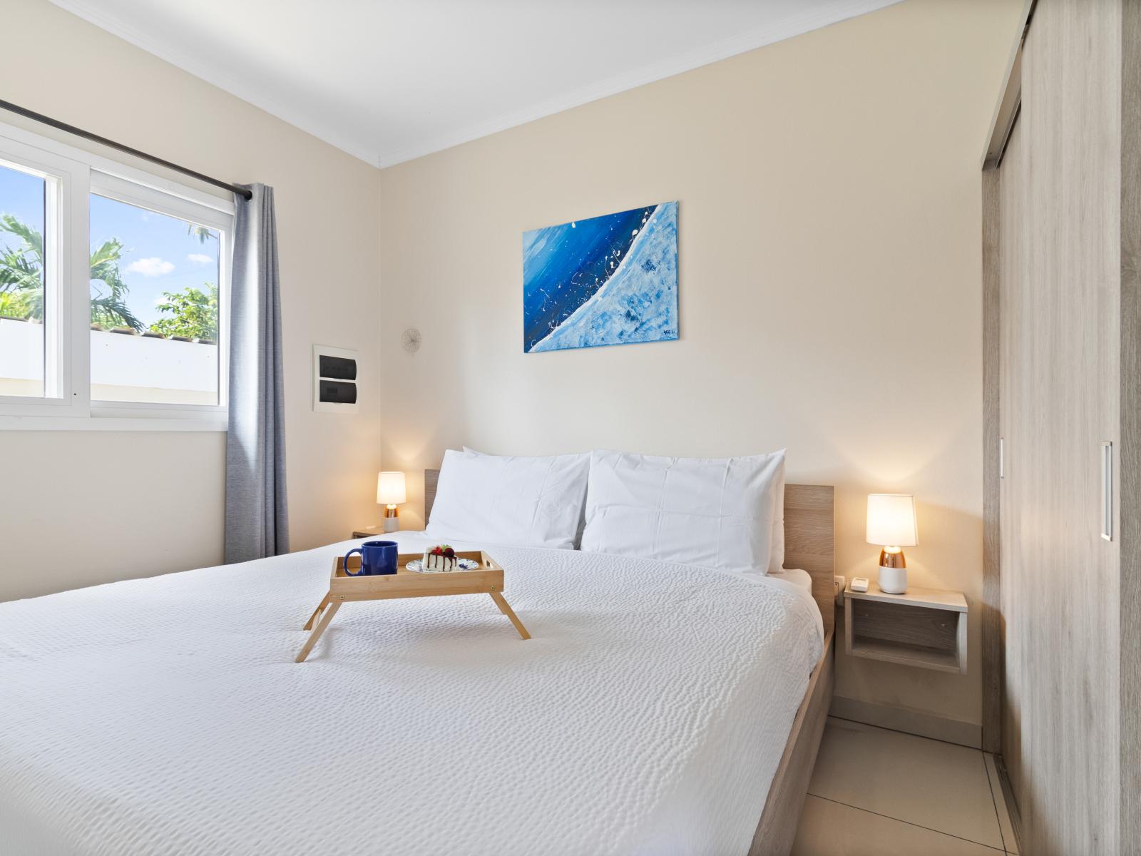 Imposing bedroom of the apartment in Noord, Aruba - Comfy king size bed - Elegantly designed room beautifully decored with large aesthetic wall paintings - Majestic table lamps - Neat and clean linen with soft pillows - Large size bright window