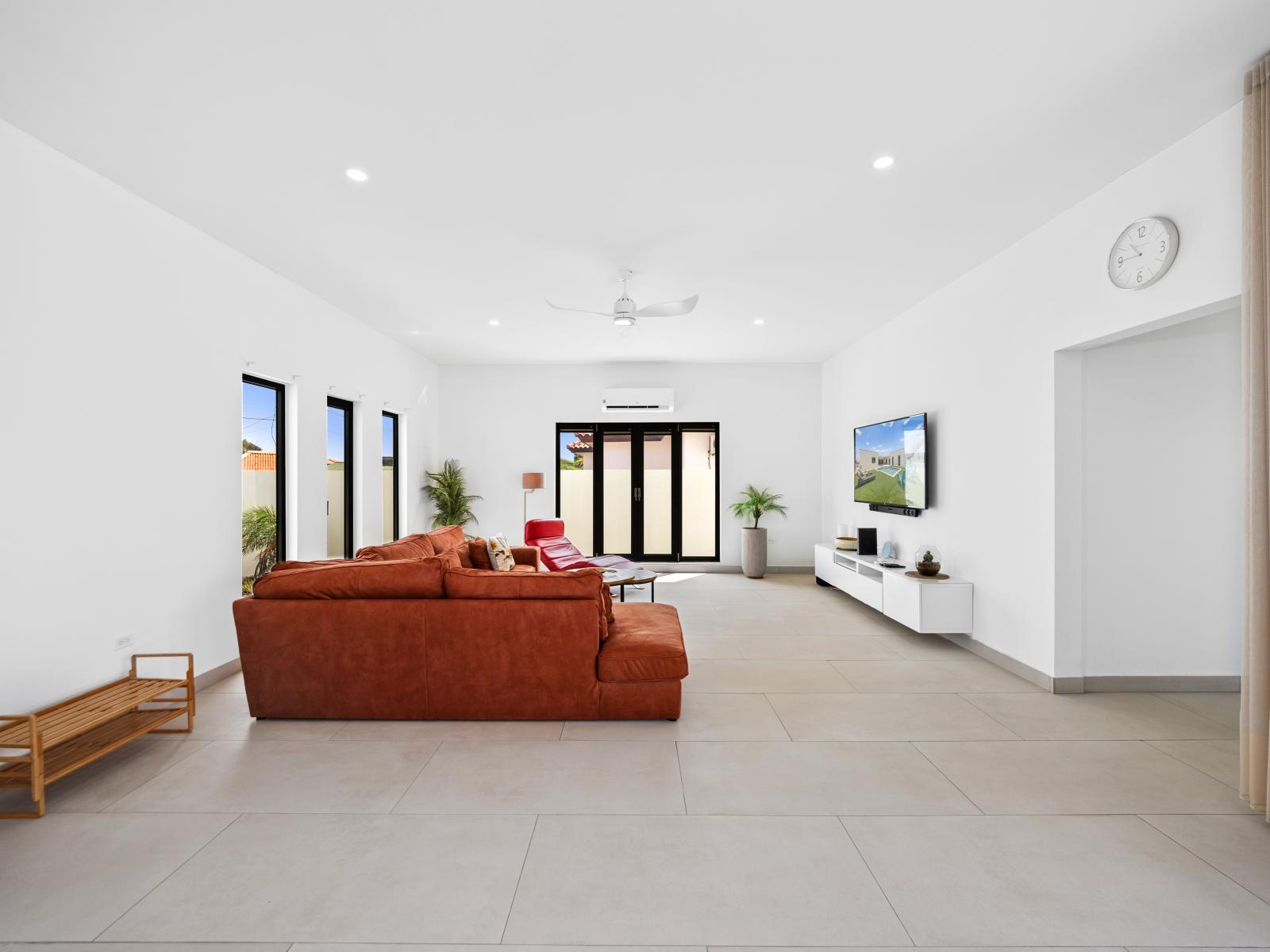 Spacious living area of the home in Noord, Aruba - Availability of wall mounted flat screen smart TV - Cozy sofas to relax after a day of exploration - Beautiful white themed living space with big and bright windows