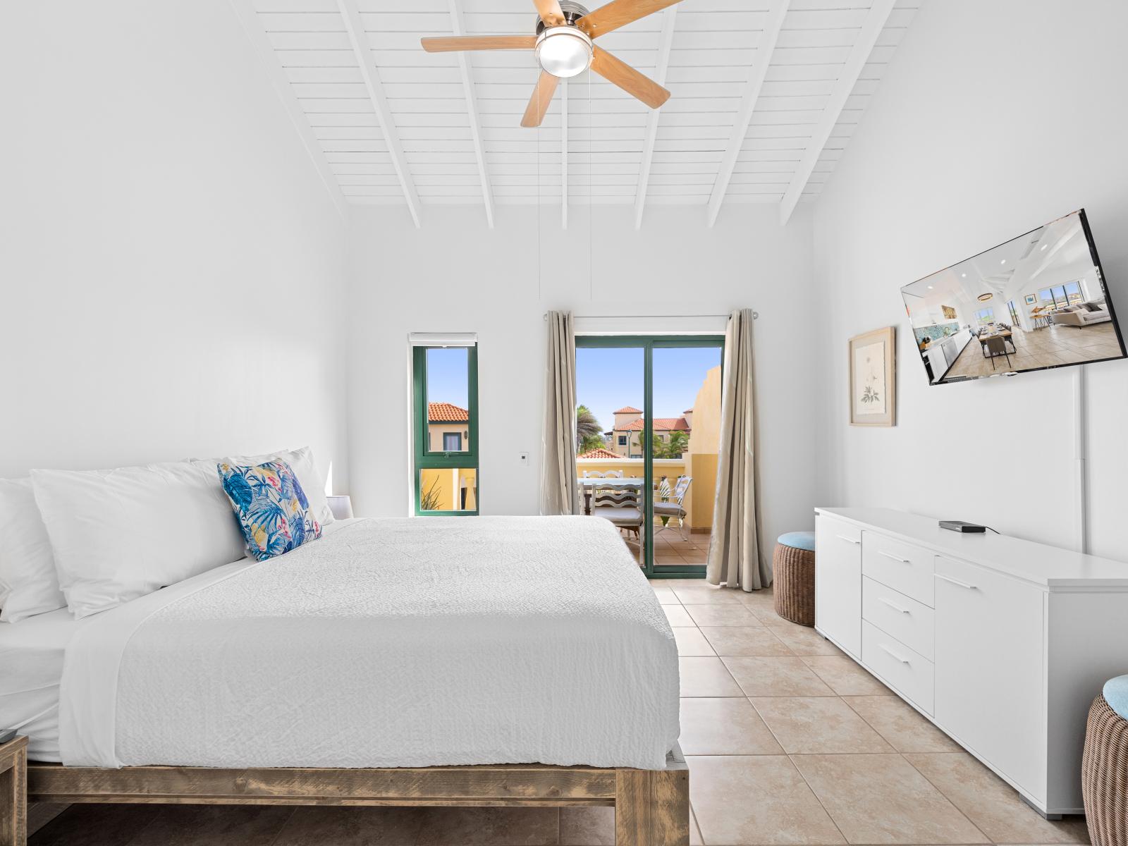 Lofty bedroom of the condo in Noord Aruba - With access to the balcony through glass sliding doors - Clean lines and minimalist design for a calming atmosphere - Smart TV and Netflix - A tranquil ambiance perfect for unwinding and rejuvenating