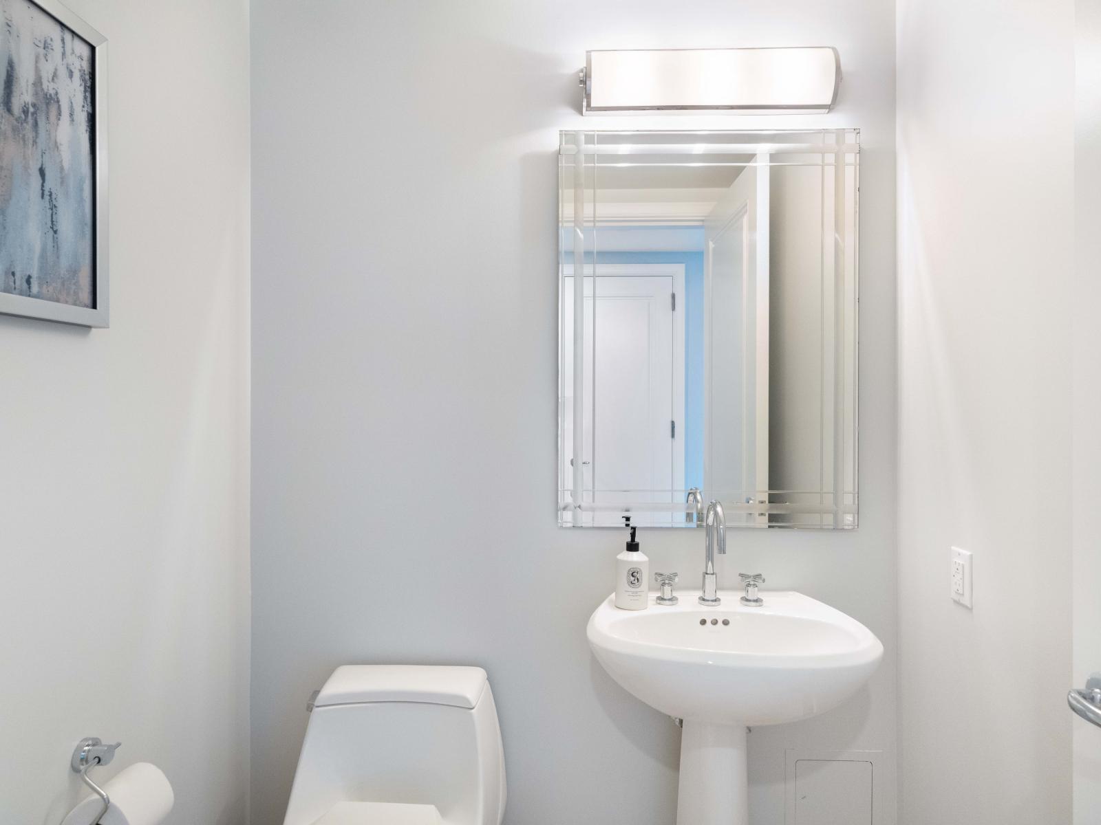 Sophisticated Sanctuary: Indulge in Style and Comfort in Our Miami Condo's Half Bathroom, complete with Designer Lighting, a Generous Mirror, and Pristine Amenities.