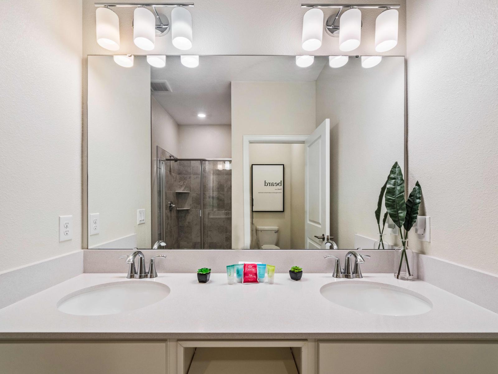 High-Class Bathroom of the Condo in Kissimmee - Glorious Twin sink Vanity with large size wall mirror - Stunning Lamps above the mirror - Neat and clean cozy toilet seat - Outstanding and stunningly tiled Glass Cabin shower area