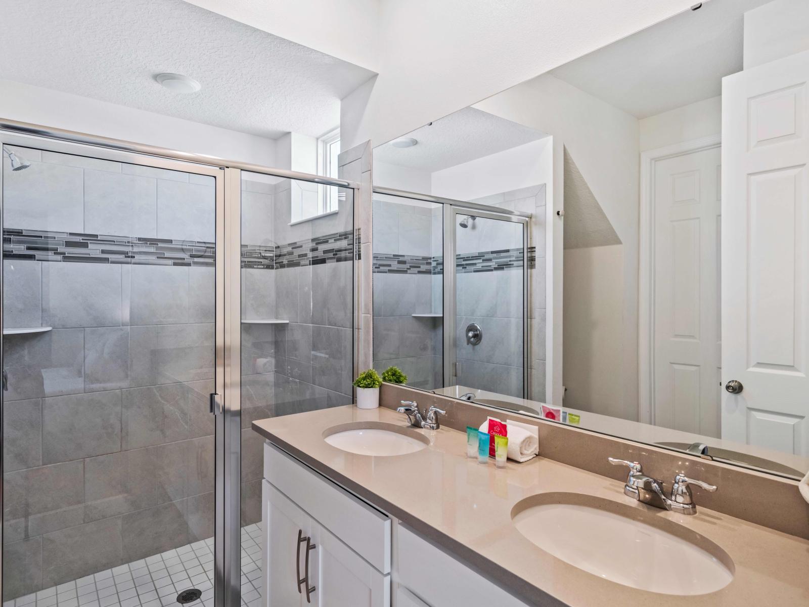 Premium bathroom in the Kissimmee home, boasting a spacious vanity area - Immaculate toilet seat for hygiene and comfort - Stunning glass-enclosed shower space - Elegantly tiled bathroom with sophisticated lighting, enhancing the overall aesthetic