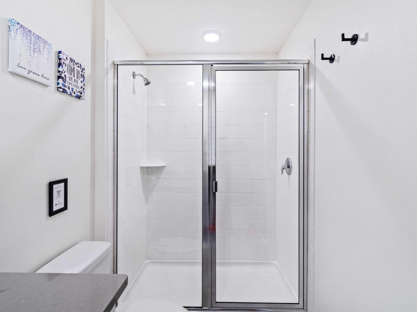 Unwind in a spacious walk-in shower area of bathroom of home in Kissimmee - Adorned with sleek fixtures and indulgent amenities - equipped with a rainfall showerhead and soothing jets - Spacious layout and glass walls create an inviting ambiance