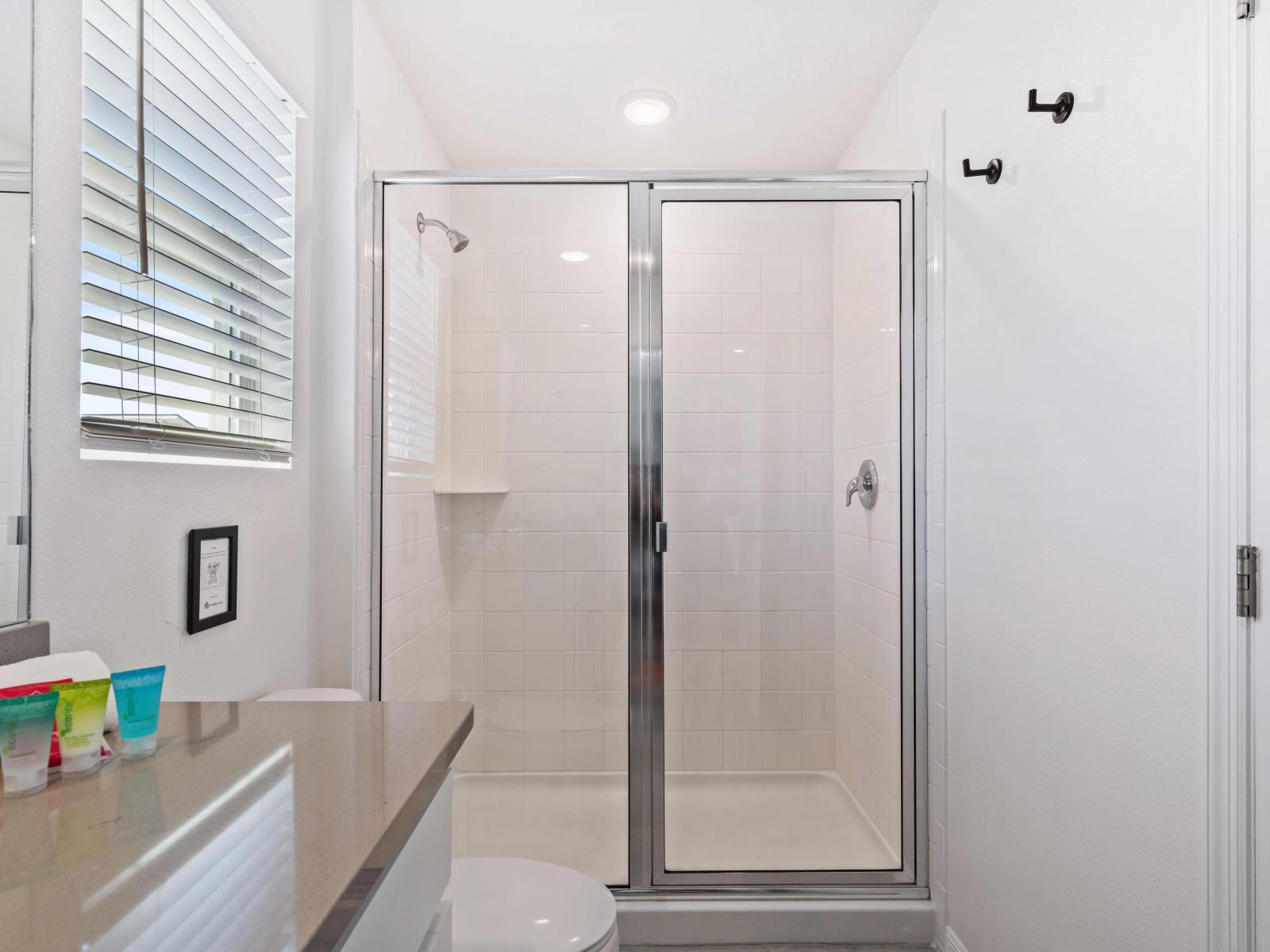 Unwind in a spacious walk-in shower area of bathroom of home in Kissimmee - Adorned with sleek fixtures and indulgent amenities - equipped with a rainfall showerhead and soothing jets - Spacious layout and glass walls create an inviting ambiance