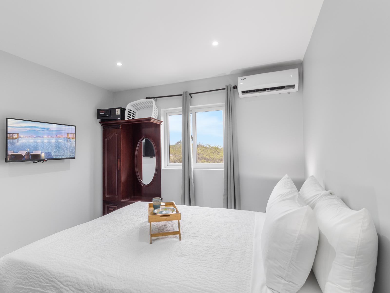 Captivating bedroom of the apartment in Oranjestad Aruba - Bedroom with a cozy ambiance, blending comfort and aesthetics - Wall mounted flat screen smart TV - Window with beautiful views