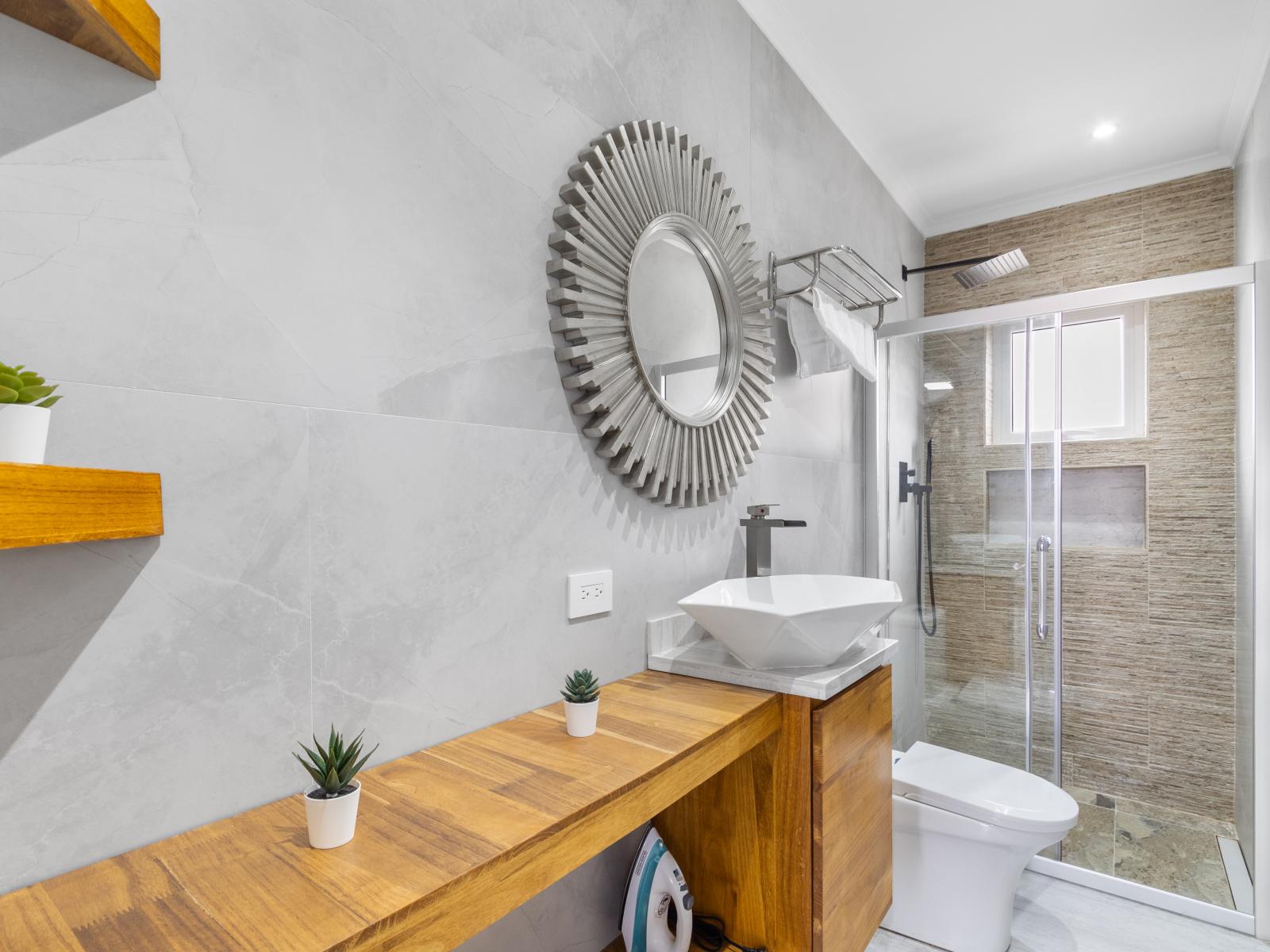 Polished bathroom  of the apartment in Oranjestad Aruba - Inviting bathroom with a soothing color palette for a tranquil feel - Glass-enclosed walk-in shower stall - Chic vanity with stylish mirror