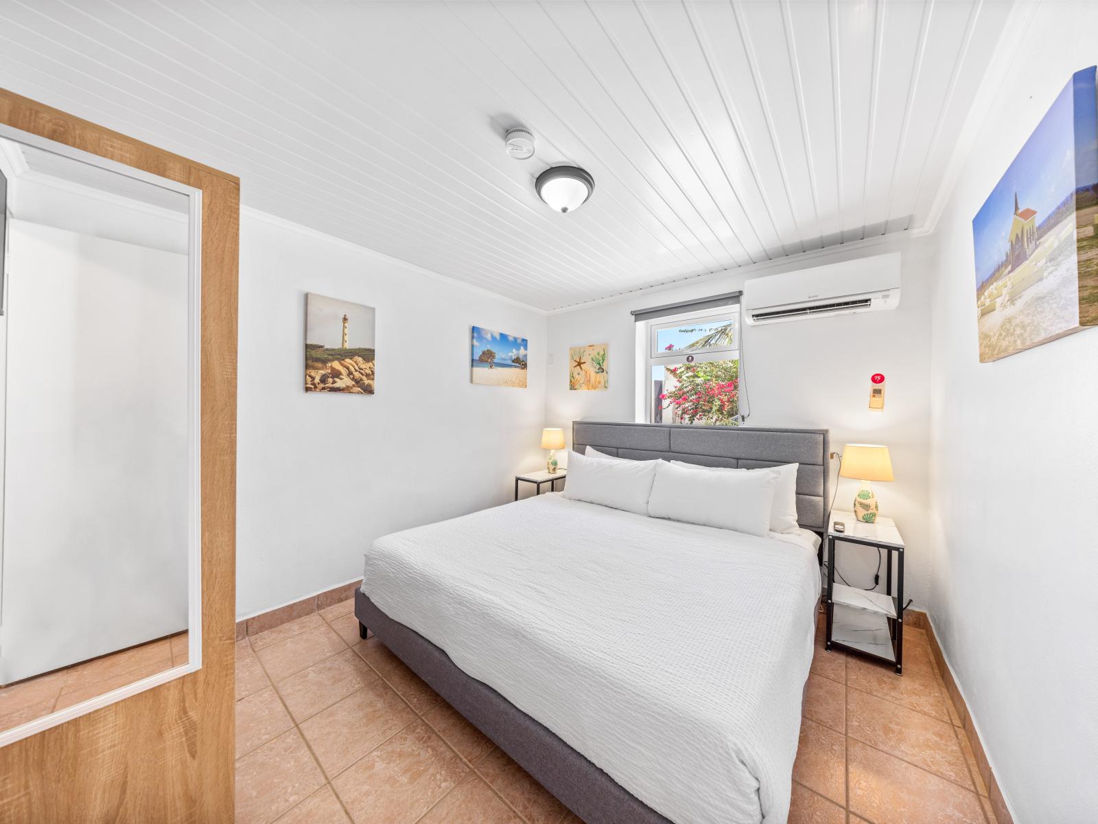 - Bedroom features a comfortable king-size bed with crisp white linens for a restful sleep - Room is equipped with an air conditioner, perfect for unwinding and relaxing - Airy ambiance with natural light from the window, creating a serene atmosphere