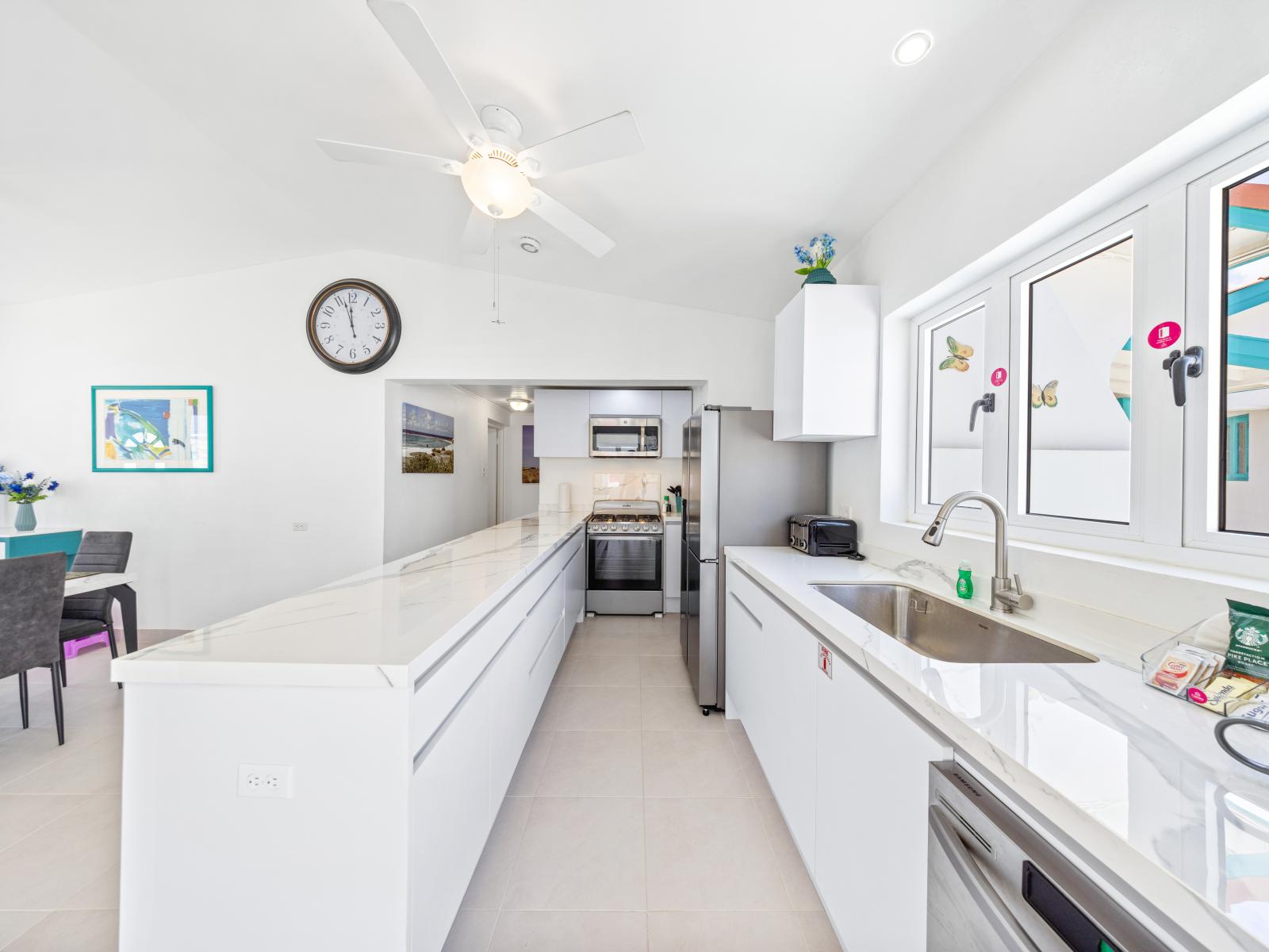 - Bright, open kitchen with modern appliances and plenty of counter space for cooking - Sleek, white cabinetry adds a touch of elegance, complementing the vibrant decor - Large windows invite natural light, creating a warm and inviting atmosphere