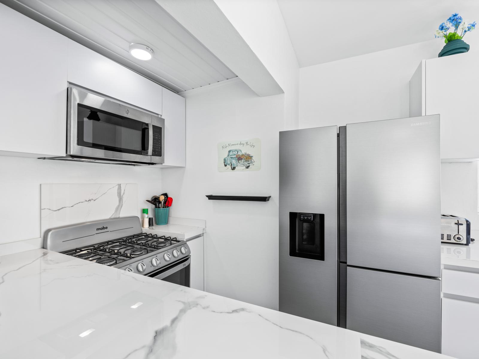 - Sleek and modern kitchen equipped with a stainless steel refrigerator and microwave - Spacious countertops with a marble-like finish, perfect for meal prep       - Contemporary design with a clean aesthetic that invites you to cook in style