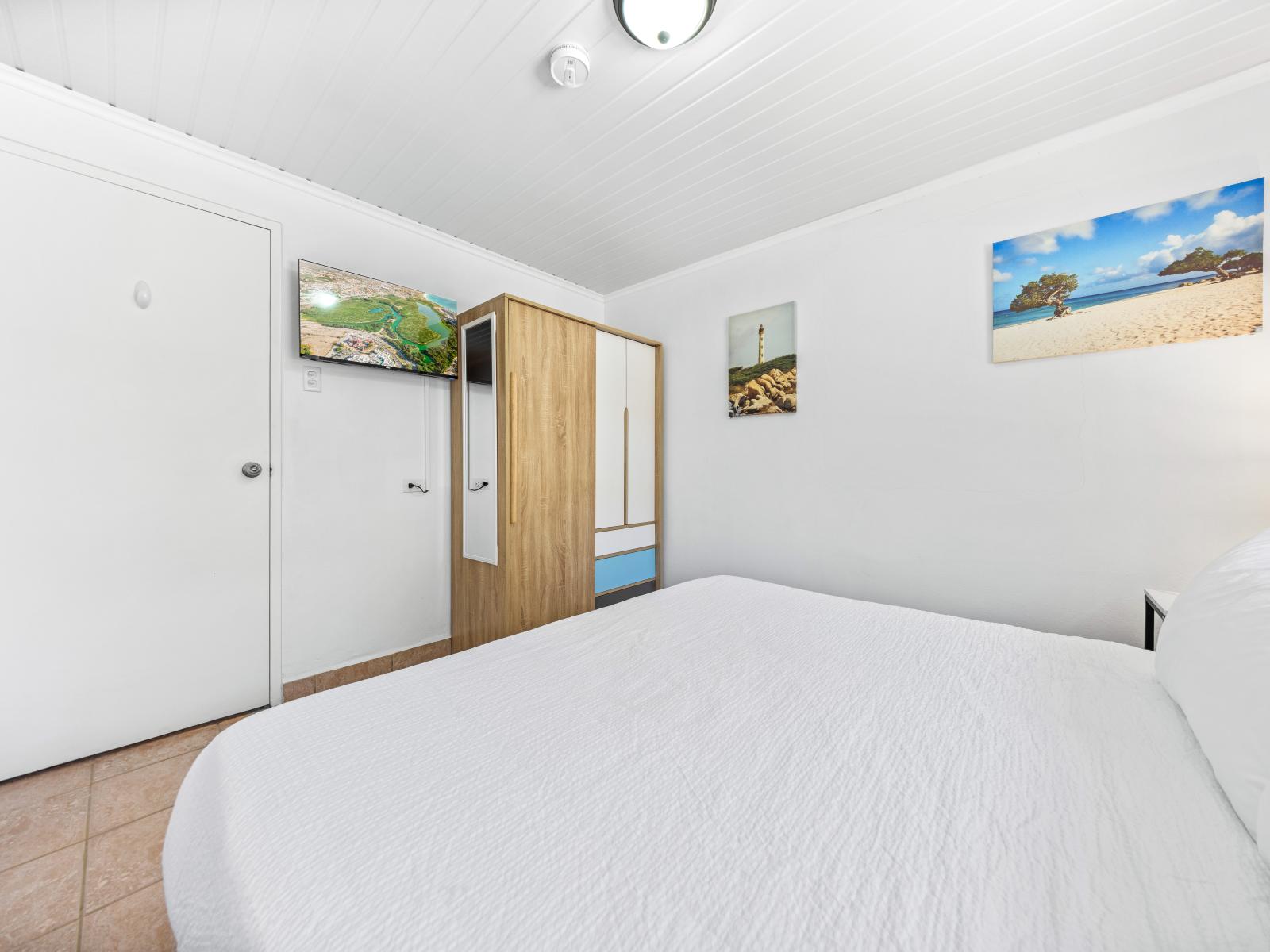 - Cozy bedroom with a comfortable king-sized bed and soft linens - Wall-mounted TV for entertainment, perfect for winding down after a day in the sun - Modern decor with beach-themed artwork, creating a relaxing and serene atmosphere