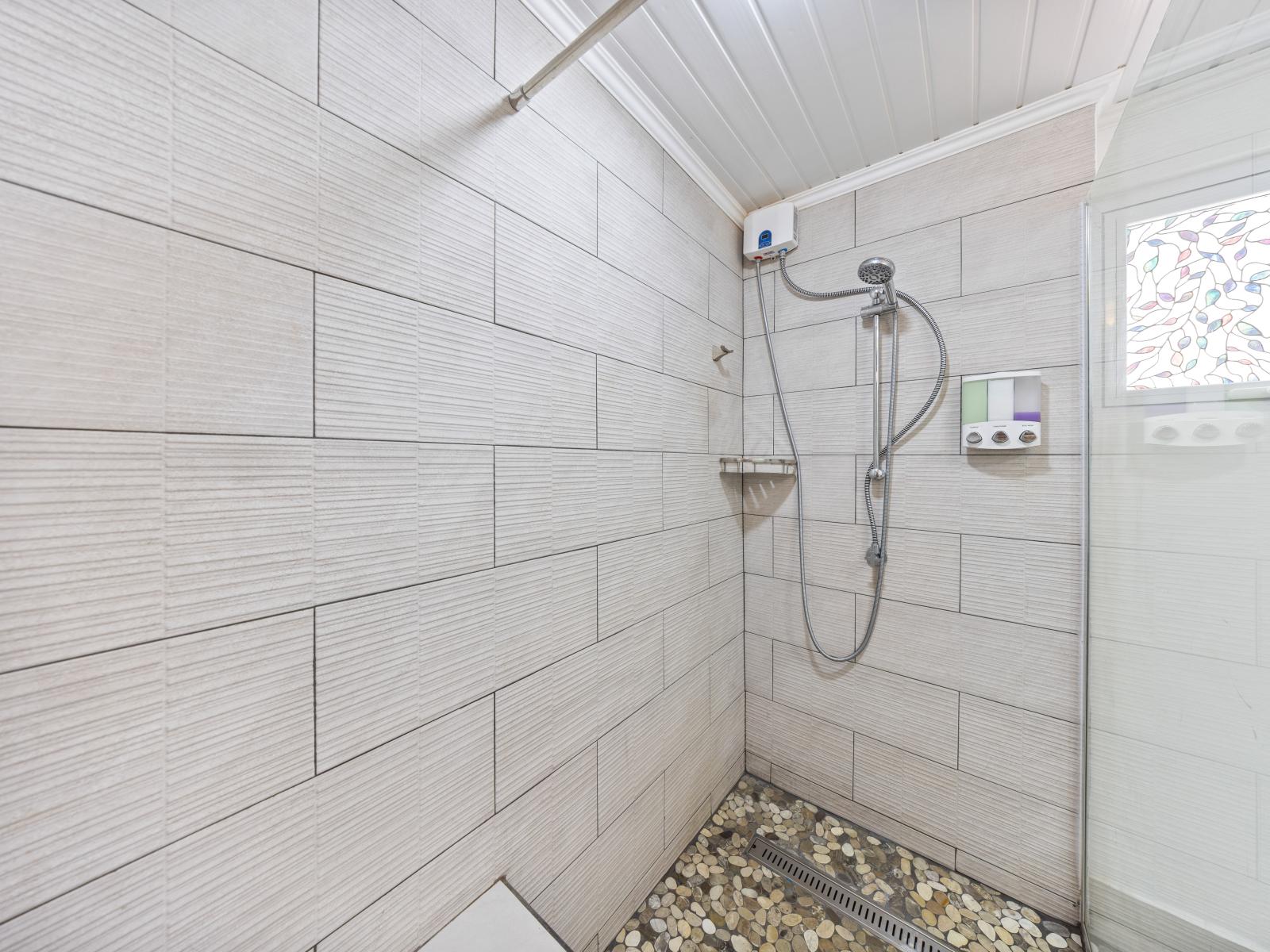 - Spacious walk-in shower with a rainfall showerhead for a peaceful experience - Elegant tile design and pebble stone flooring create a calming atmosphere - Enjoy the perfect blend of style and function in this modern walk-in shower space