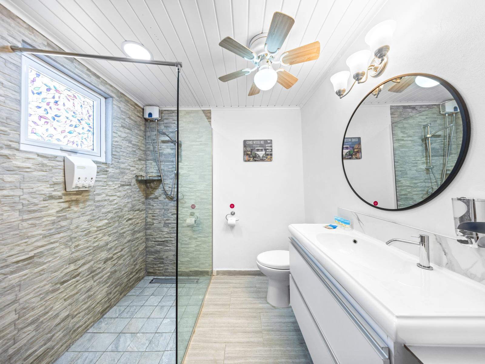 - Spacious bathroom with a modern walk-in shower and stylish glass partition - Large vanity mirror and plenty of countertop space for your toiletries for a peaceful stay - Contemporary design with natural light filtering through a decorative window