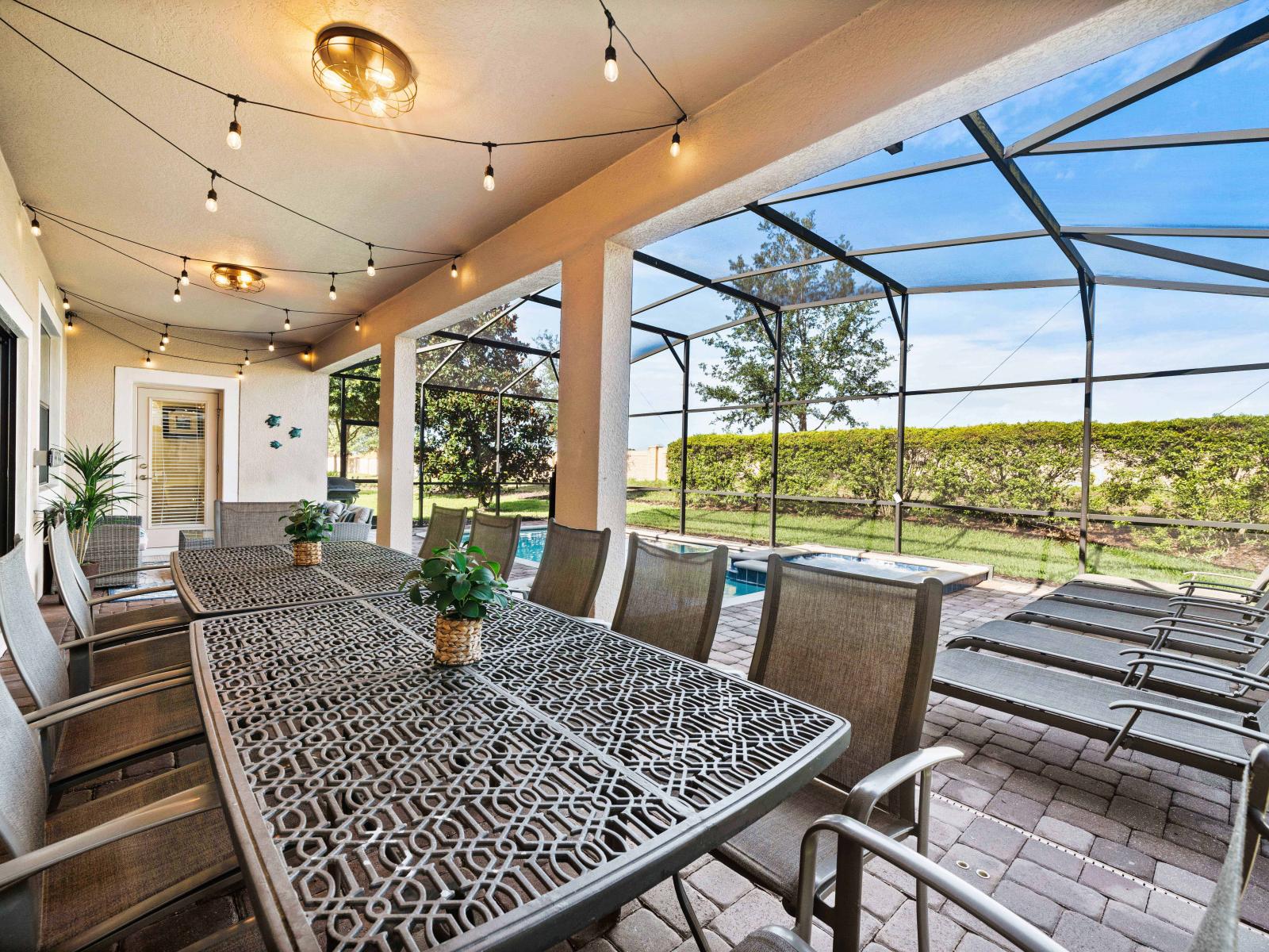 Spacious outdoor dining area with elegant seating, perfect for hosting gatherings - Covered patio with string lights, creating a cozy ambiance for evening events - Scenic view of the private pool and backyard through a screened enclosure