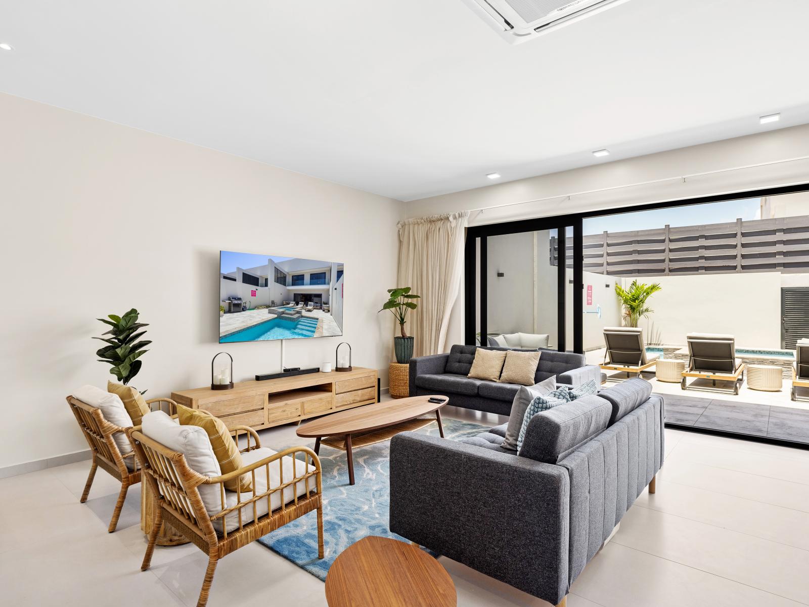 Entertain and unwind in spacious living area of the apartment in Noord Aruba - Thoughtfully curated decor and plush seating creating a warm and welcoming atmosphere - Offering a flat screen wall mounted smart TV and easy access to outdoor with pool