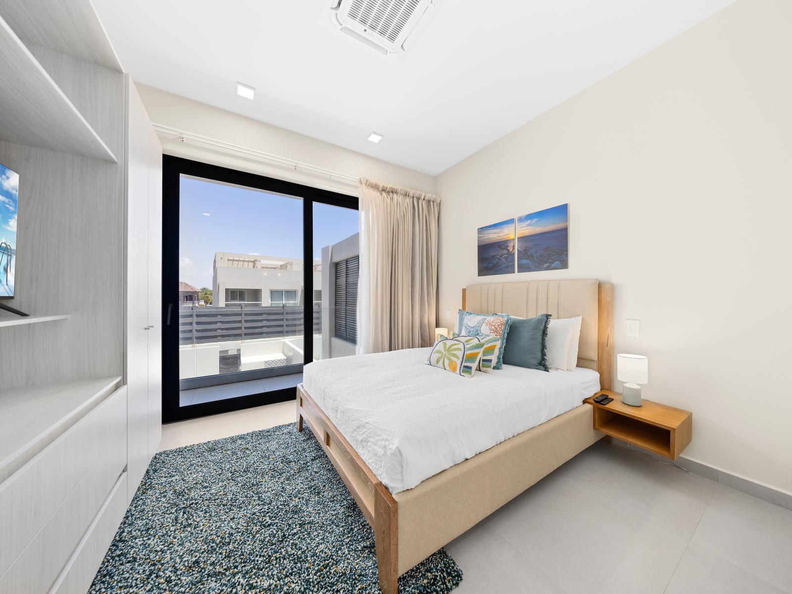 Discover serenity and sophistication in well-appointed bedroom of the apartment in Noord Aruba - Smartly organized space offering a queen size bed and access to balcony with sliding glass door - Minimalistic approach ensuring a clean space to relax