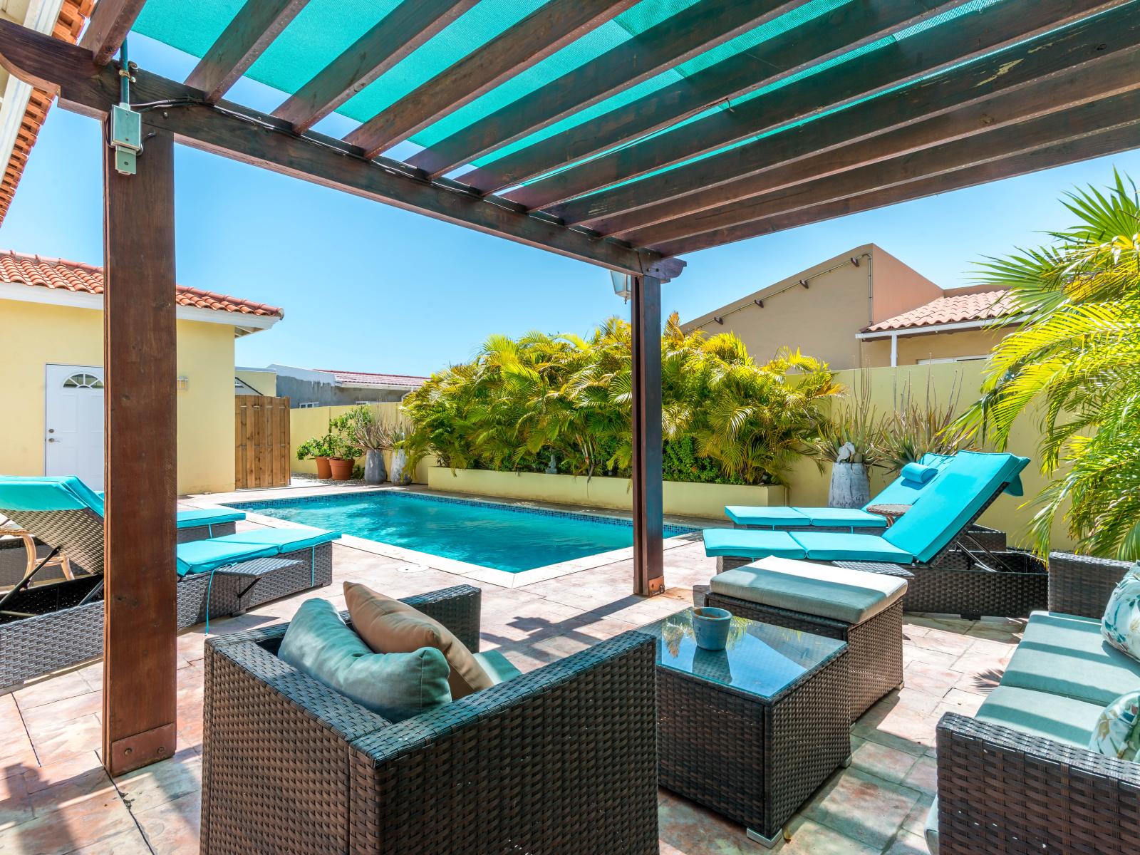 Unwind and relax in the fresh air of cozy outdoor seating of the home in Noord Aruba - Shaded outdoor seating area by the private pool - Create unforgettable memories under the open sky in welcoming outdoor seating setup