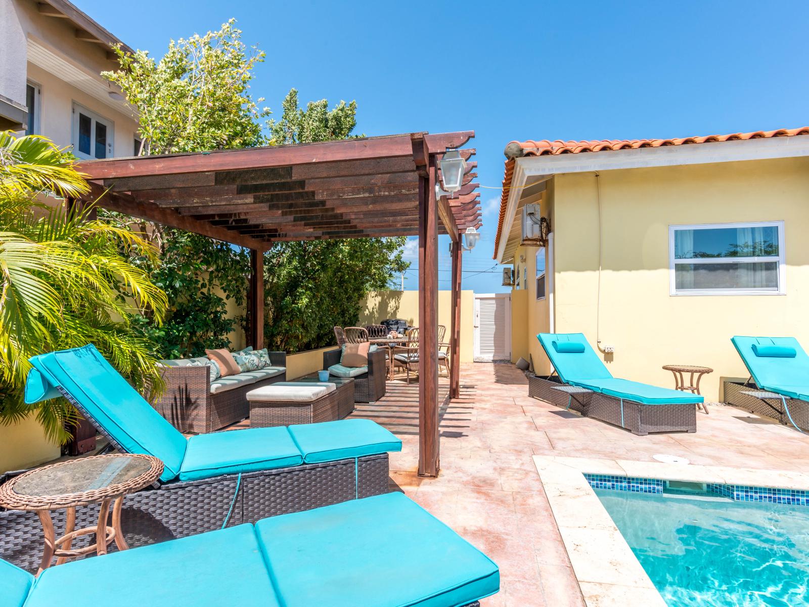Enjoy the tranquility of the outdoors from the comfort of outdoor seating area of the home in Noord Aruba - Lots of chairs by the pool for laying in the sun with pool views - Bask in sun-kissed luxury near the water and unwind