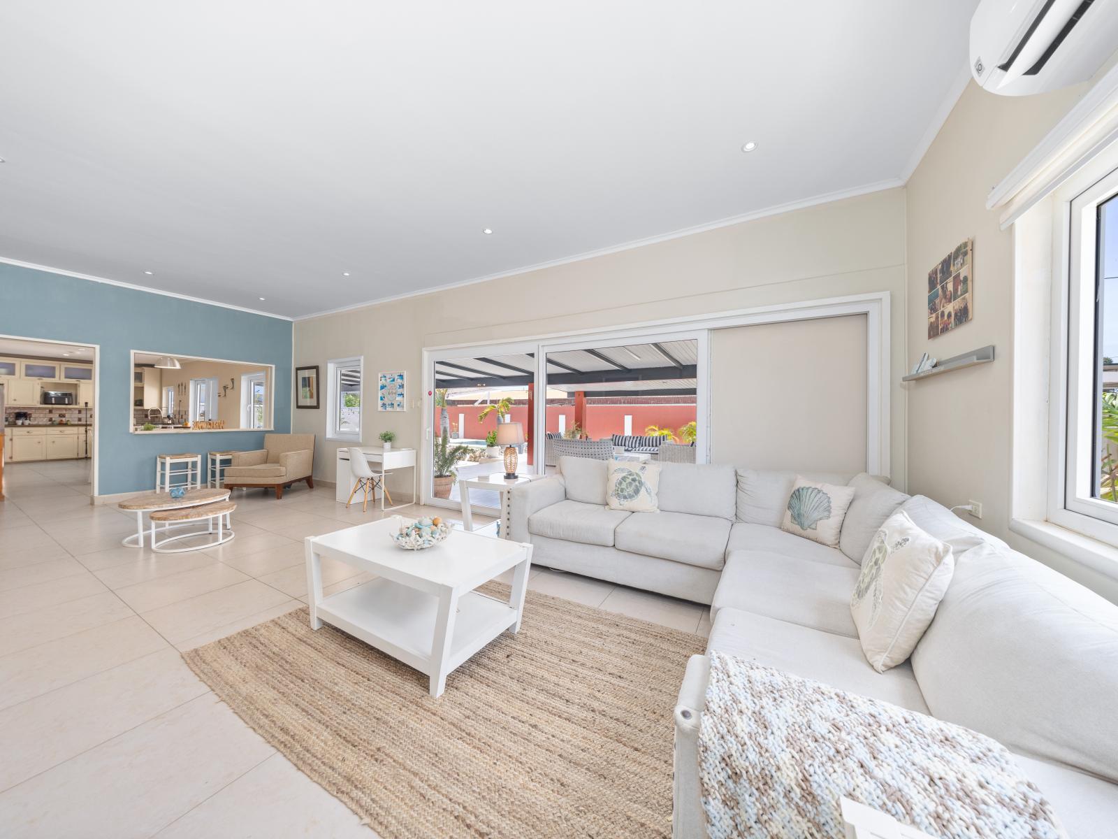 Highlighting the open plan living area of the home in Oranjestad, Aruba - Emphasizing the large windows that allow natural light to flood the room - Showcasing plush sofas and armchairs that provide plenty of seating with availability of smart TV