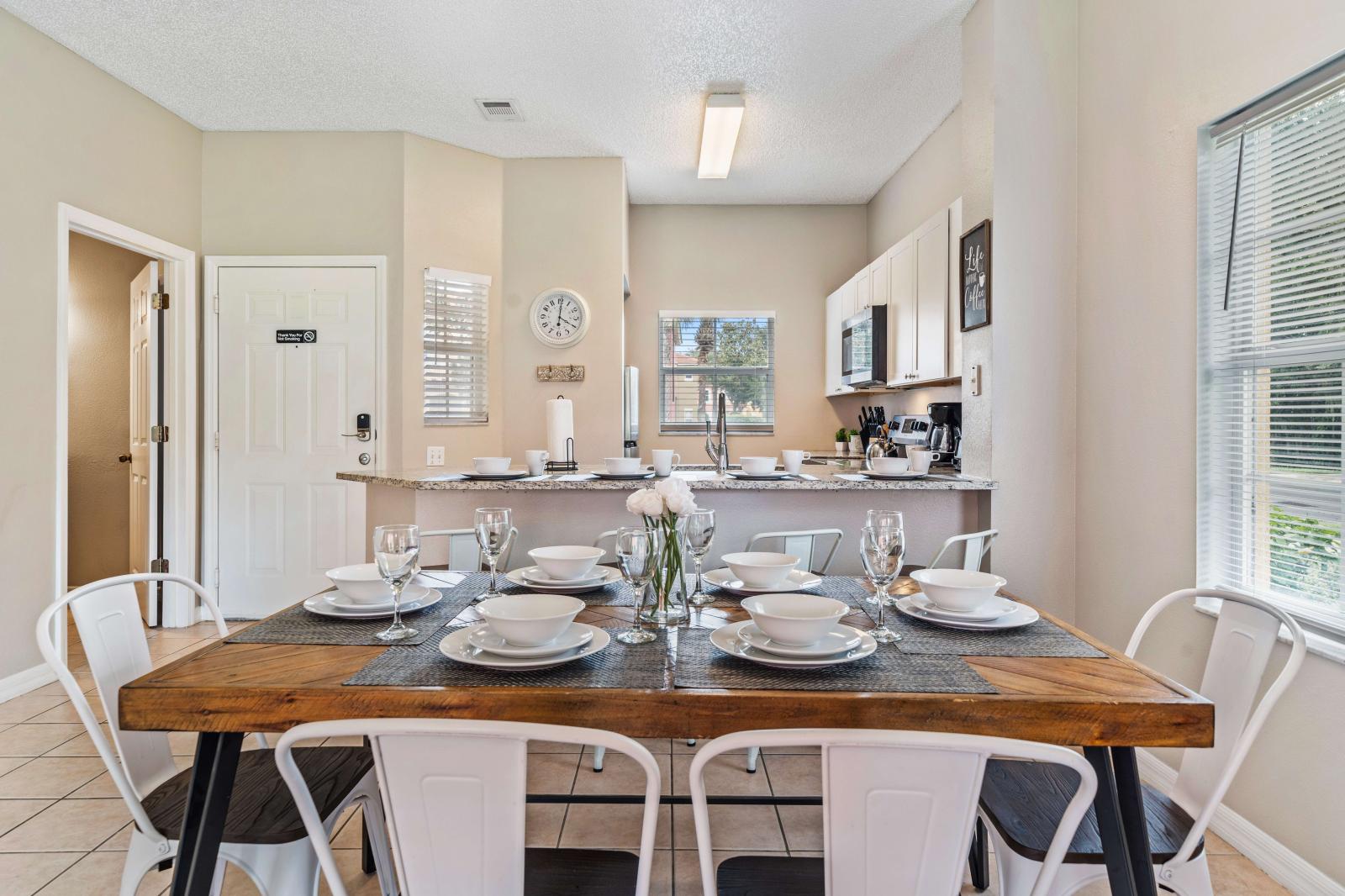 Gather around the spacious dining area, which offers seating for six persons - Rustic wooden dining table is elegantly set with stylish place settings, creating a warm atmosphere - Large windows fill the room with natural light enhancing open feel