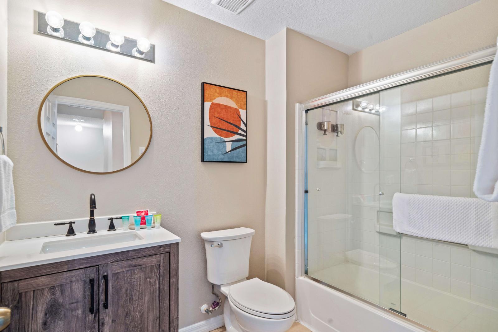 This stylish bathroom features a contemporary vanity with a round mirror and modern lighting - Includes a sleek glass-enclosed shower, perfect for a refreshing shower - Thoughtfully decorated with modern artwork and equipped with the essentials