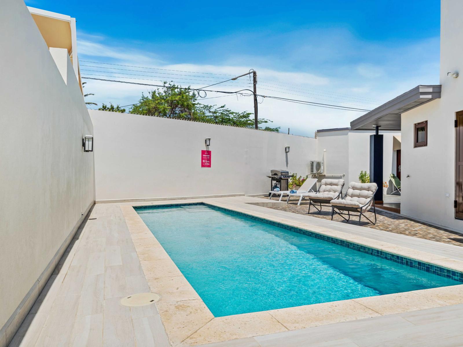 The backyard features a sleek, pool with crystal-clear water, perfect for relaxing or swimming laps - Lounge chairs and a barbecue area provide a perfect setting for outdoor gatherings - Enclosed by walls, the area ensures privacy and tranquility