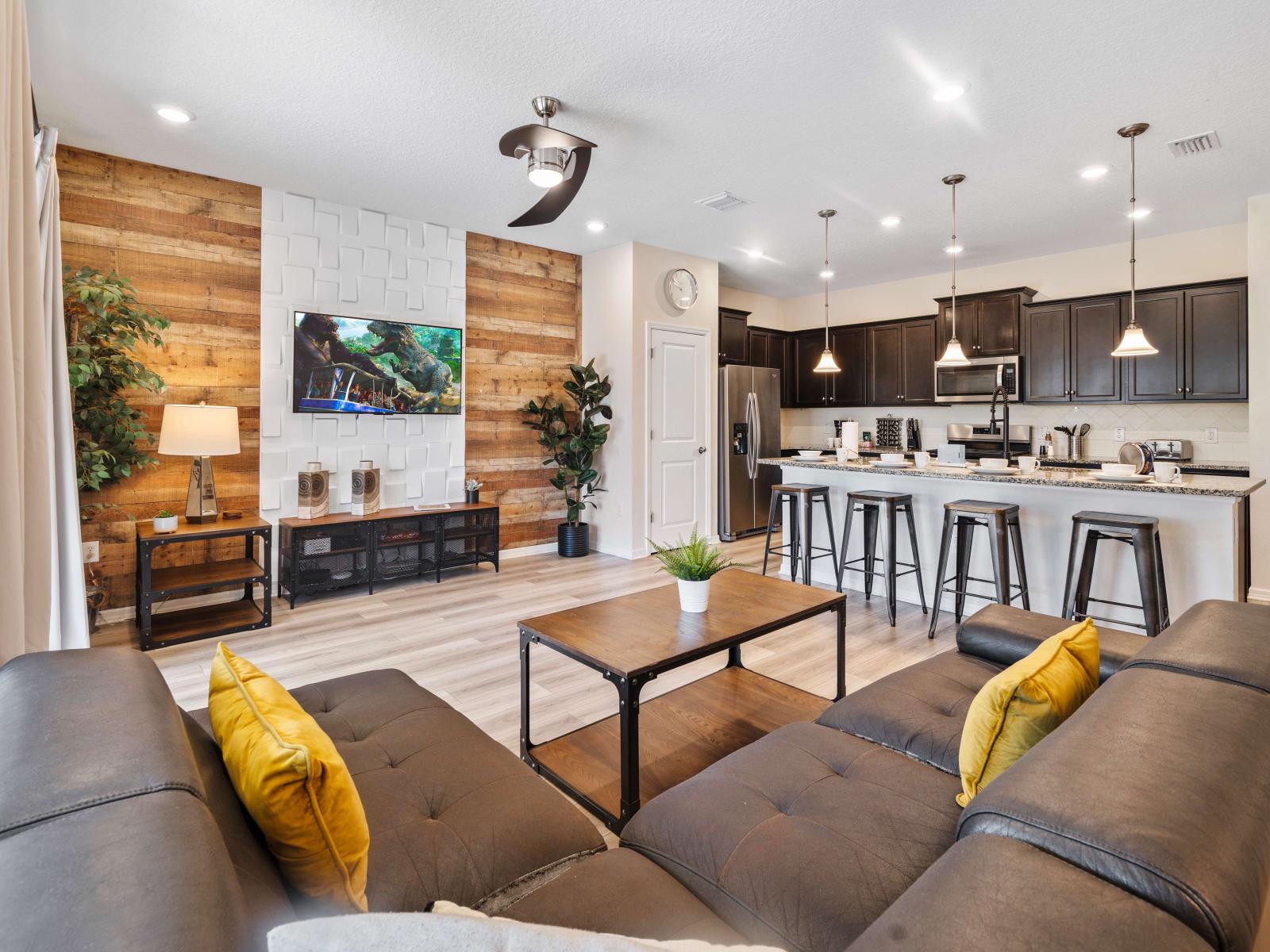 Inviting living room featuring a black sectional, vibrant yellow pillows, and a smart TV on a stylish accent wall - Contemporary open kitchen with a roomy island and sleek bar stools, perfect for casual dining and socializing