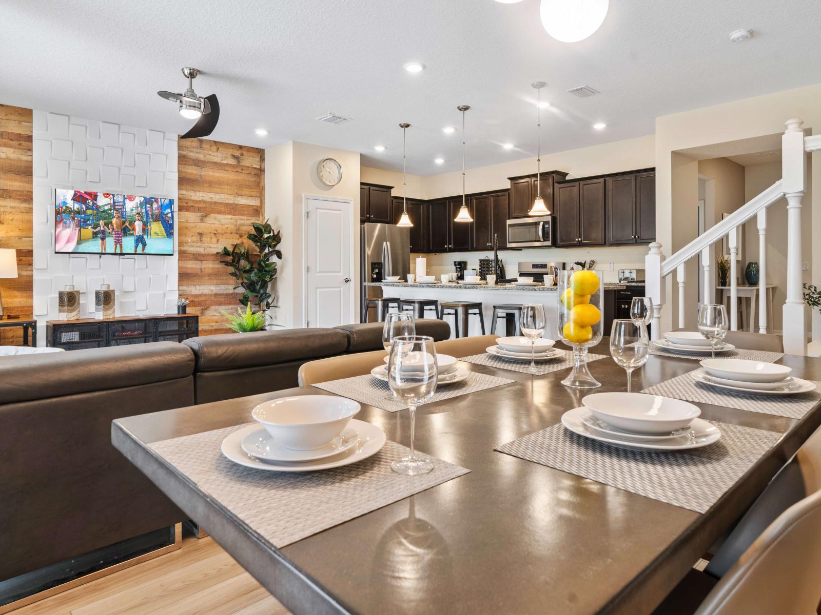 The dining area boasted by light fixture, and a sleek table set with elegant dishware and smart TV for entertainment - Connected open kitchen with a spacious island and bar stools - An elegant staircase with clean lines connects to the upper floor