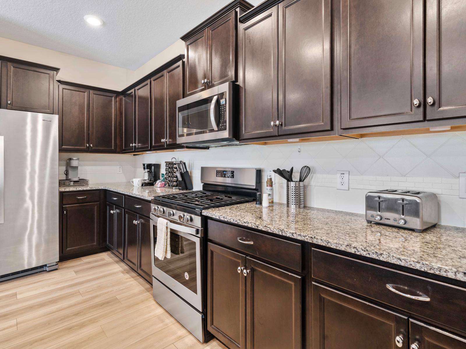 The kitchen boasts sleek stainless steel appliances and rich dark wood cabinets - Granite countertops, and cabinet space ensures a clutter-free space - Neatly organized cooking utensils make this kitchen both functional and aesthetically pleasing