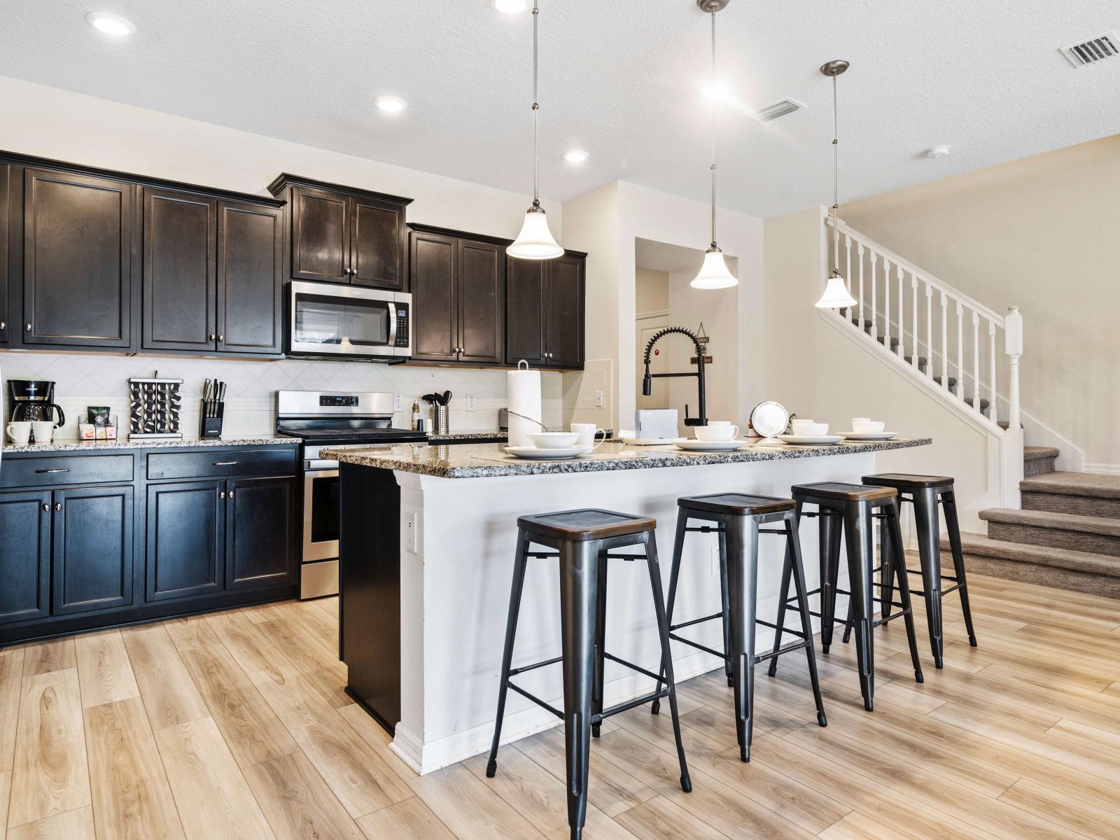 Sleek kitchen featuring stainless steel appliances, and dark wood cabinets - A spacious island with seating for four, ideal for casual dining or entertaining - Modern pendant lighting illuminates the open kitchen area, adding a stylish touch