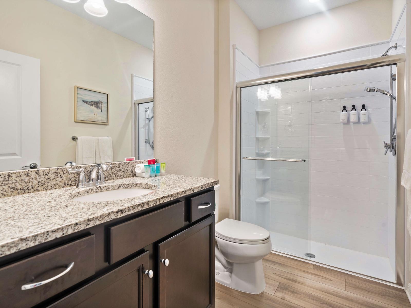 Walk-in shower with a glass door, equipped with built-in shelves and a dispenser - Countertop vanity provides space, complemented by cabinetry that offers storage - Arranged toiletries, enhance the bathroom's inviting and elegant ambiance