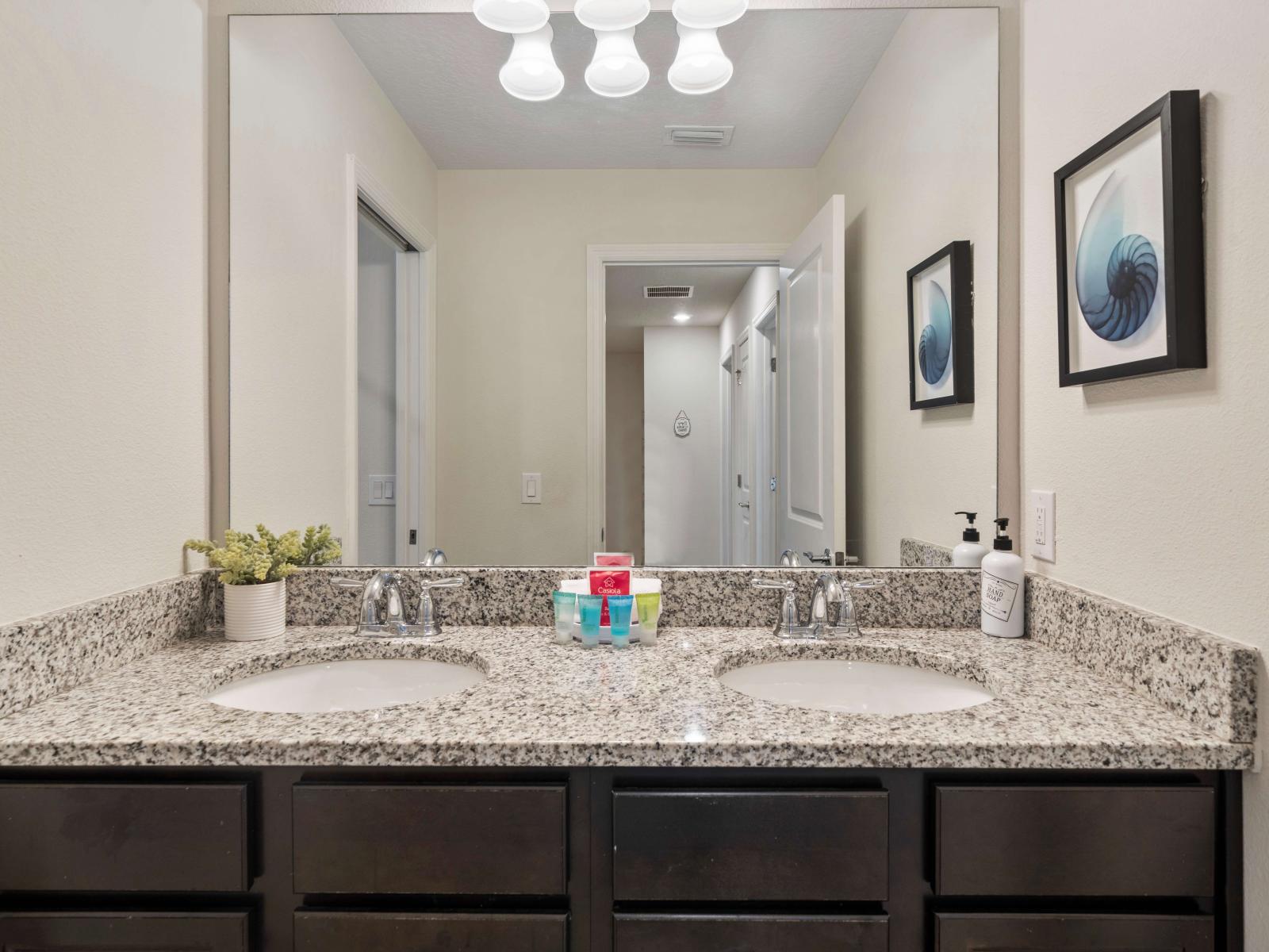 A spacious double sink vanity with elegant granite countertops and cabinetry, providing storage - The large mirror above the vanity enhances the sense of space and light - Neatly arranged toiletries, ensuring a pleasant and inviting atmosphere