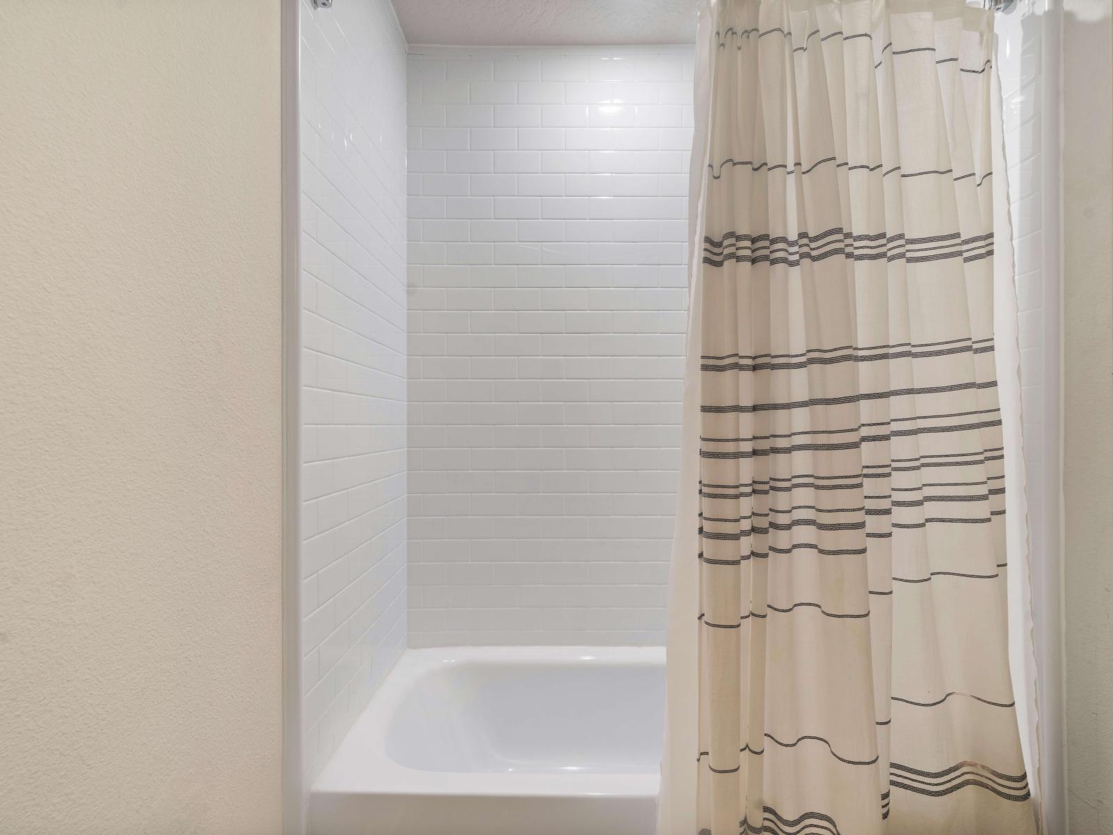 A classic bathtub and shower combo, offering flexibility for both quick showers and relaxing baths - A striped shower curtain adds a touch of style and privacy, complementing the bathroom's simple and elegant design