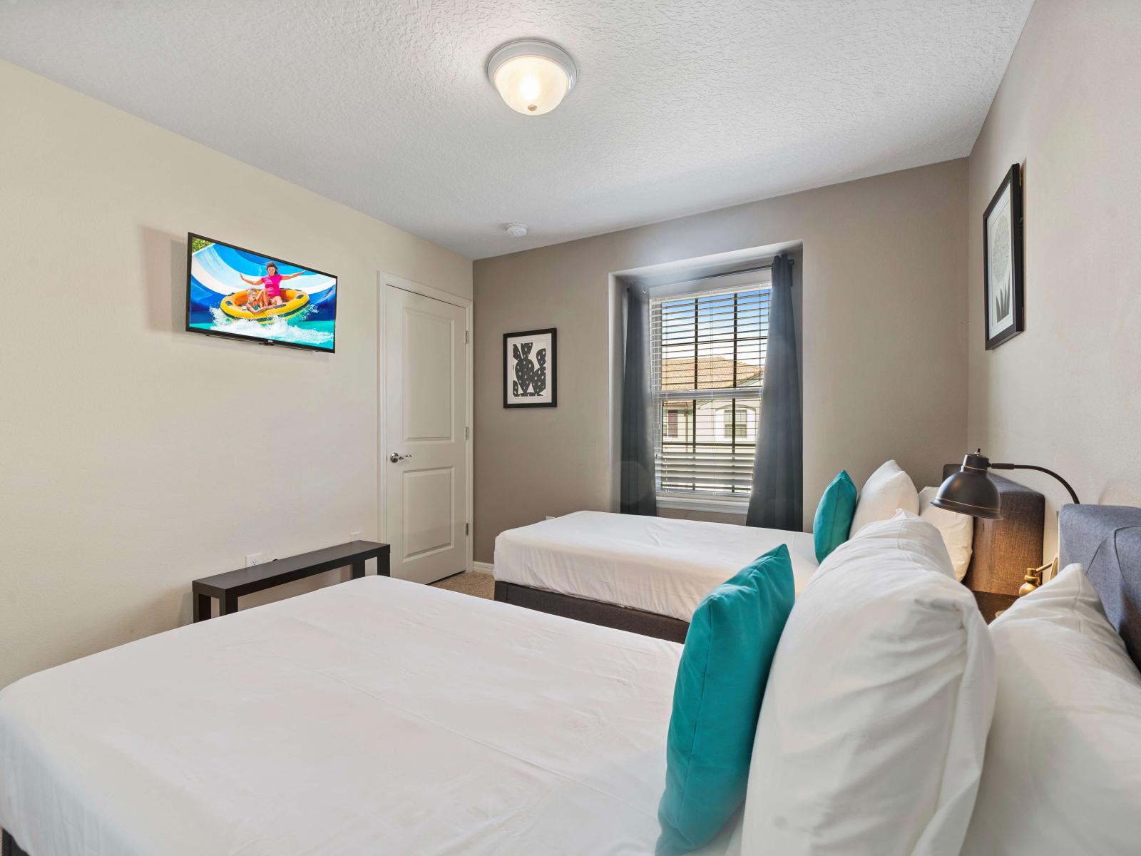 Bedroom offers two single beds adorned with vibrant accent pillows for a restful sleep - A smart TV is perfectly positioned for guests to enjoy their favorite shows and movies - Natural light fills the room, creating a warm and welcoming atmosphere