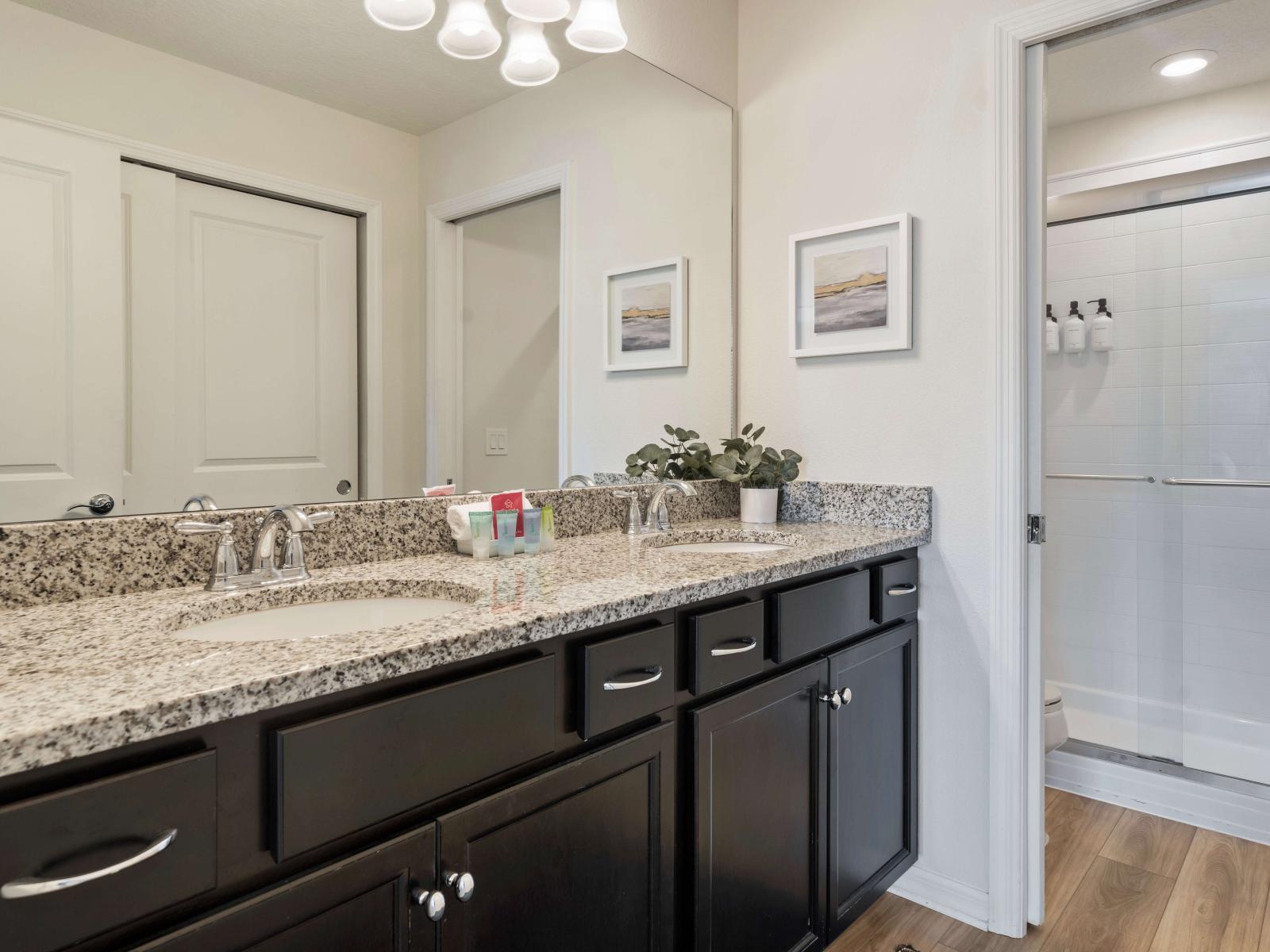 A spacious double sink vanity with elegant granite countertops and sleek dark wood cabinetry, providing storage and countertop space - The adjacent walk-in shower with glass doors, complements the overall functional design of the bathroom