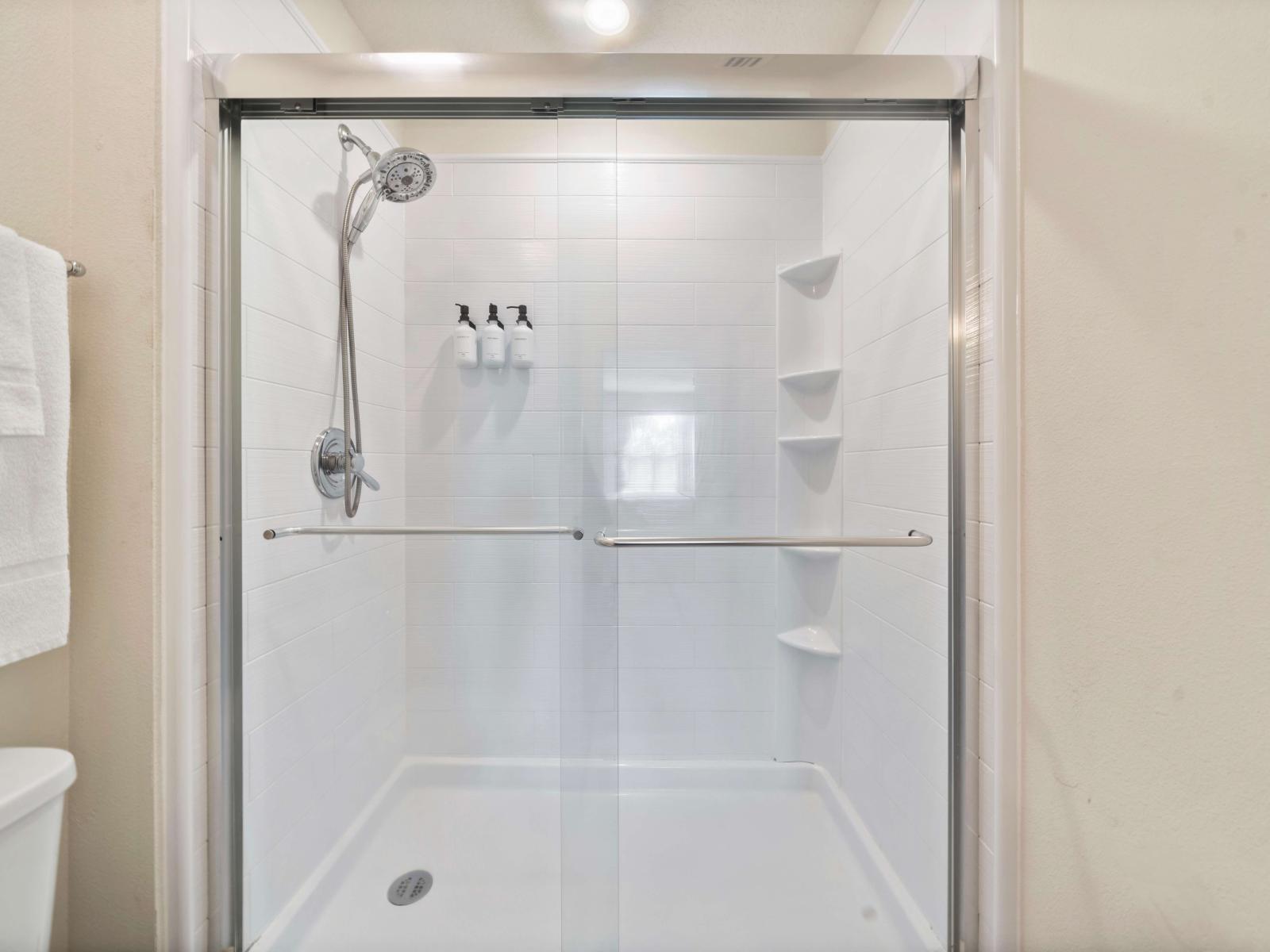 A spacious walk-in shower with a glass door, equipped with convenient built-in shelves for toiletries - The shower area includes a wall-mounted dispenser - It includes a double sink vanity, providing space for two people to use the bathroom easily