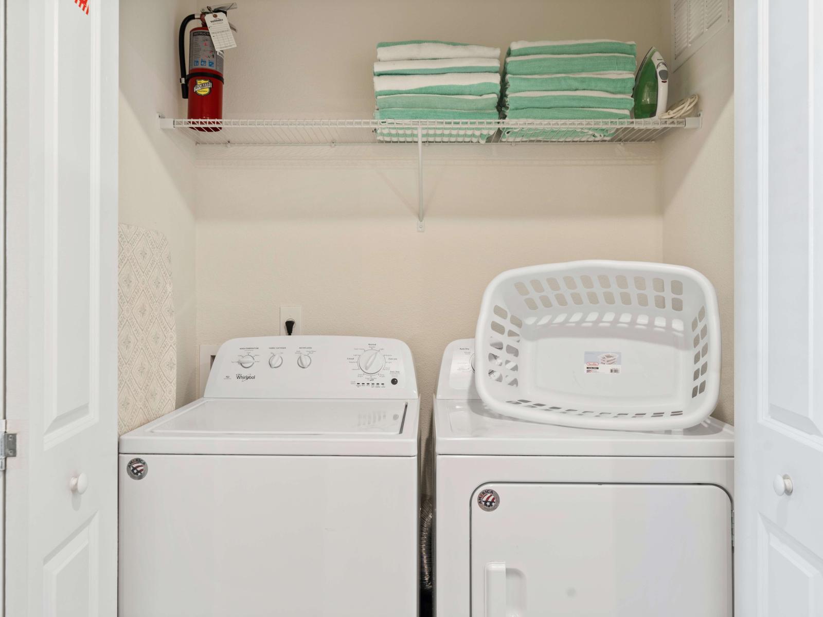 The laundry area is equipped with a washer and dryer, providing convenient in-home laundry facilities - A neatly organized shelf above holds a stack of towels, along with an iron - A fire extinguisher, ensuring both functionality and safety