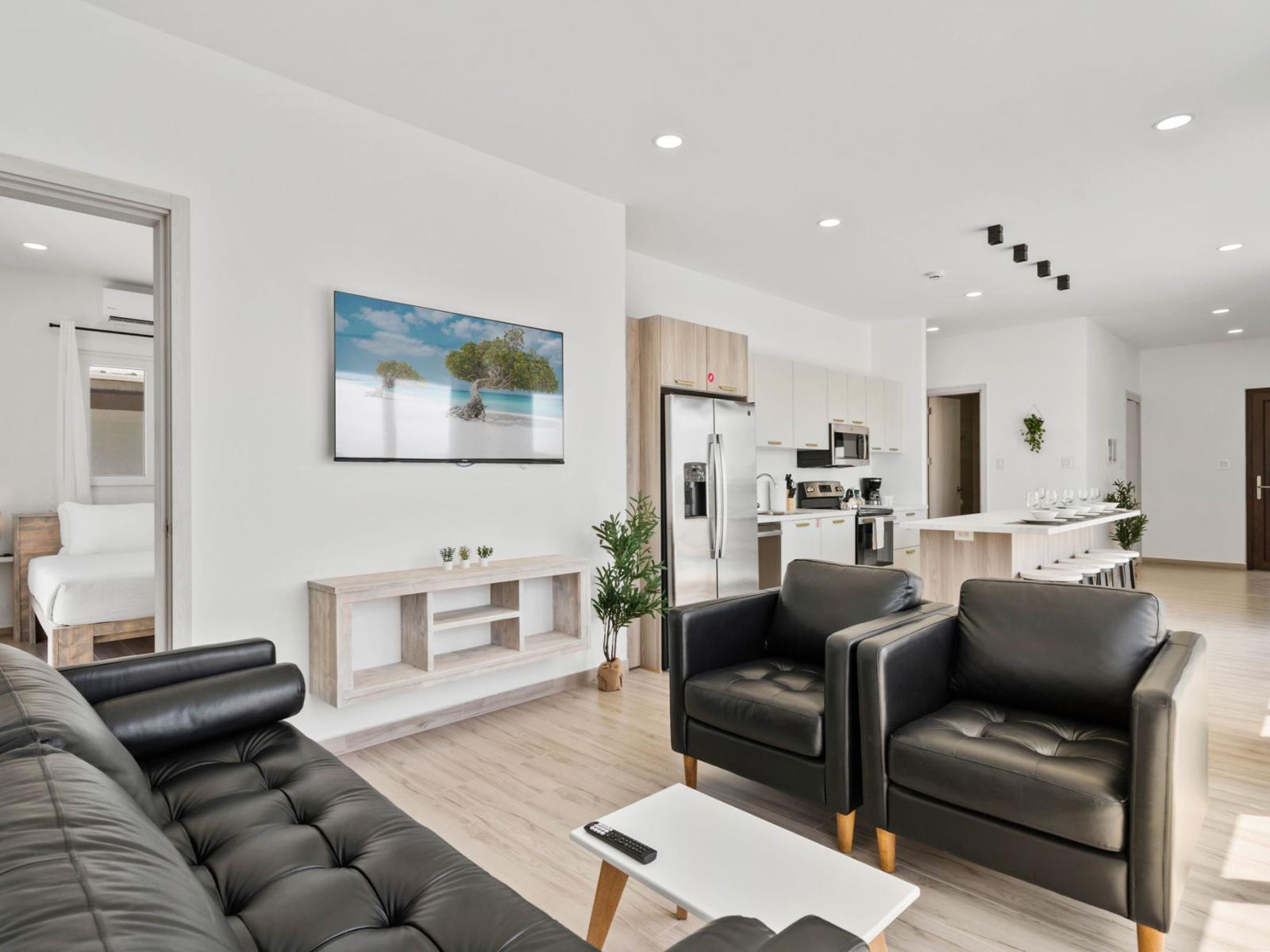 - Cozy, modern living room featuring plush leather seating and a large flat-screen TV - Cook with ease in the fully equipped, stylish kitchen with steel appliances - Seamless access to bedrooms through open-concept design for ultimate comfort