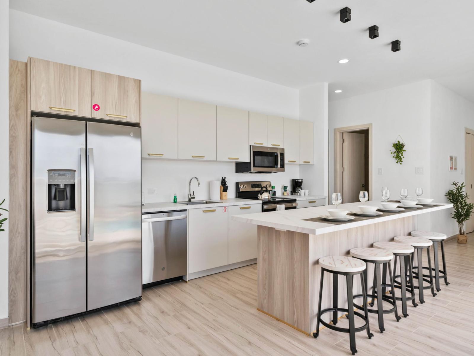 - Modern kitchen featuring stainless steel appliances and minimalist cabinetry - Spacious island with stools set for five, perfect for casual dining or entertaining - Clean, neutral tones create a bright and airy atmosphere, enhanced by natural light