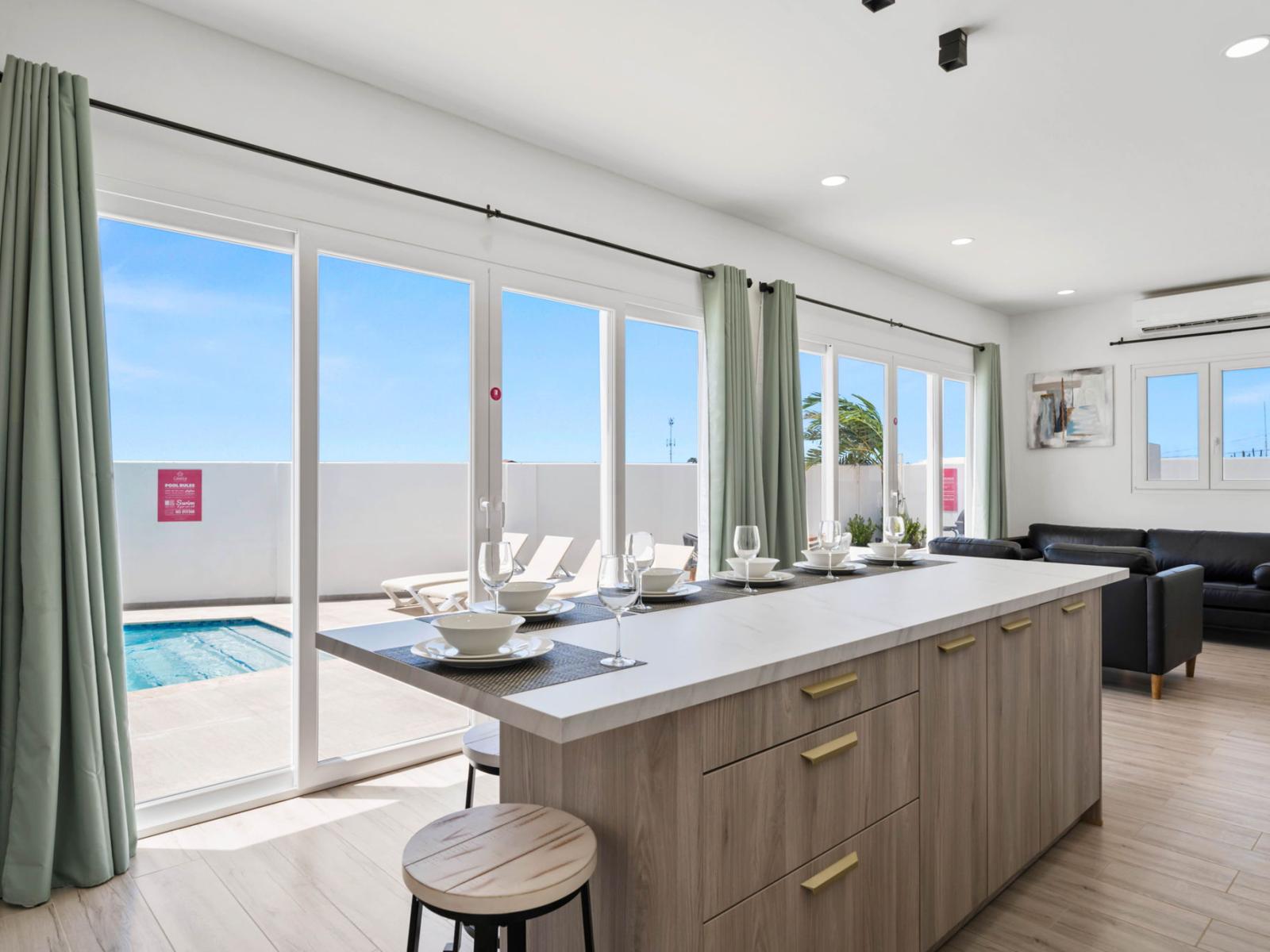 - Open kitchen with island seating overlooking a private pool through floor-to-ceiling glass doors - Natural light floods the space, creating a bright and airy atmosphere - Seamless indoor-outdoor living, perfect for relaxation and entertaining